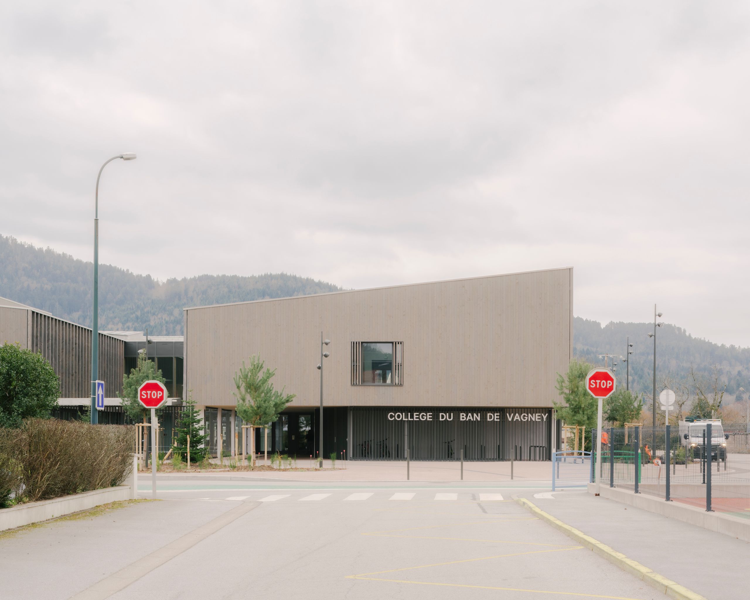 Façade principale en bois du Collège du Ban à Vagney, volume simple sur portique abritant le préau, ouvert sur le paysage boisé vosgien en arrière-plan.