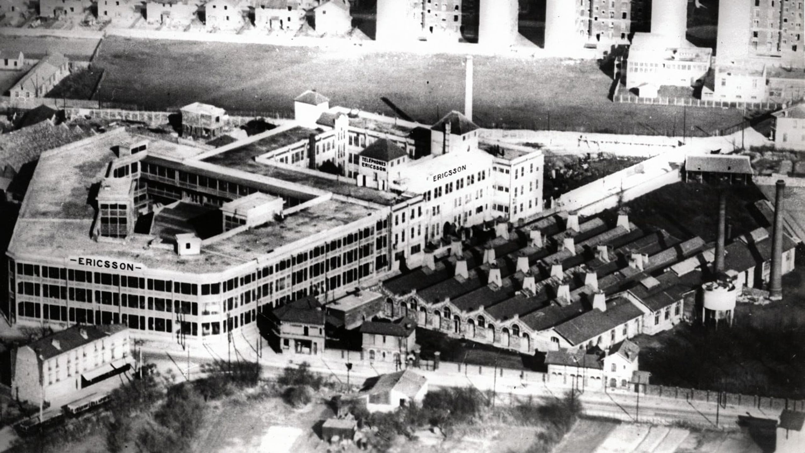 Vue aérienne historique du site industriel Ericsson à Colombes, vaste ensemble bâti en U et sheds alignés, inséré dans un tissu urbain en mutation.