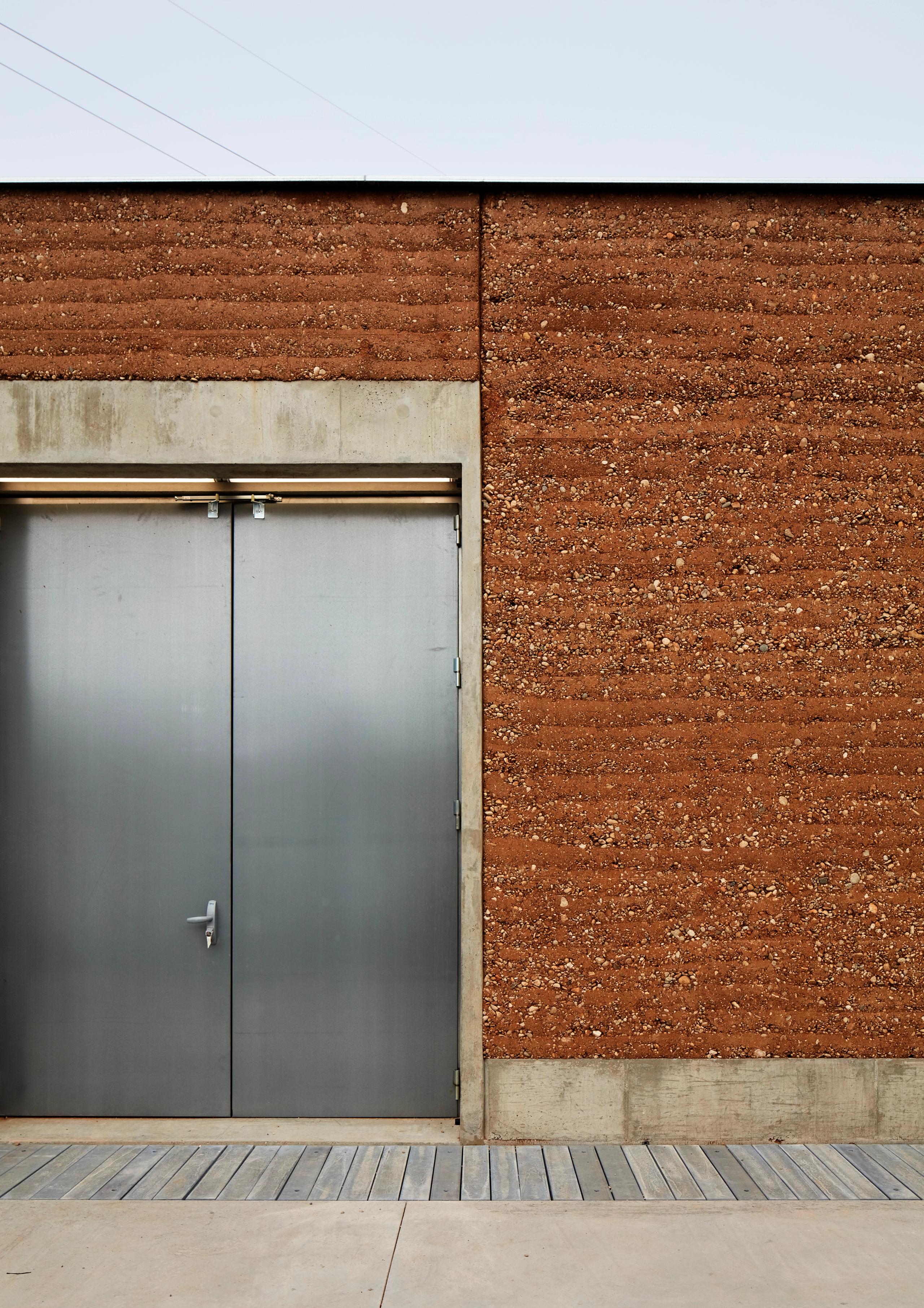 Poste source de Cusset à Villeurbanne : façade en pisé et béton brut, porte technique en acier galvanisé, composition sobre et industrielle.