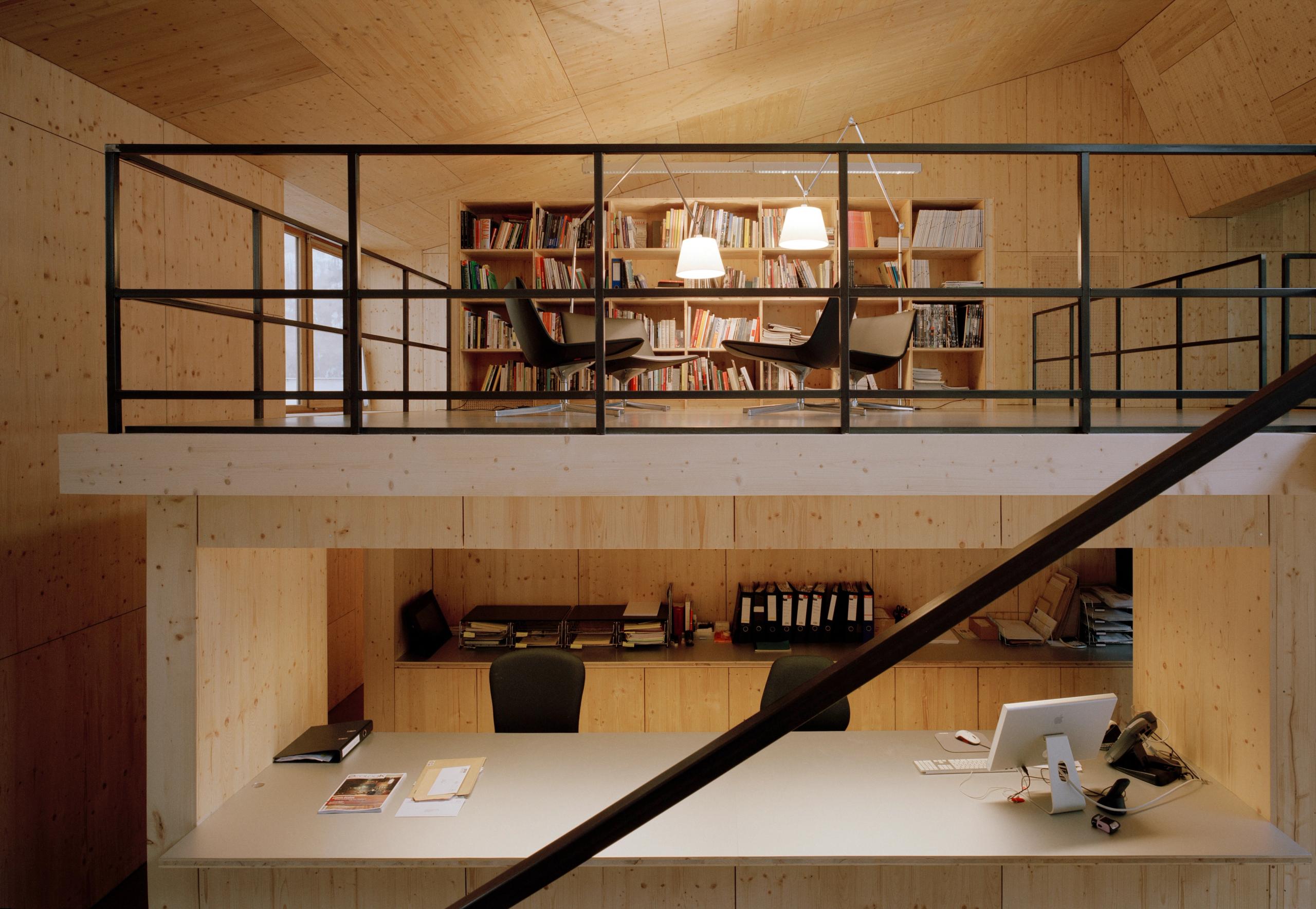Réhabilitation d’un local d’activité à Lyon par Tectoniques : plateau de travail en bois avec mezzanine bibliothèque, structure apparente et lumière nord diffuse.