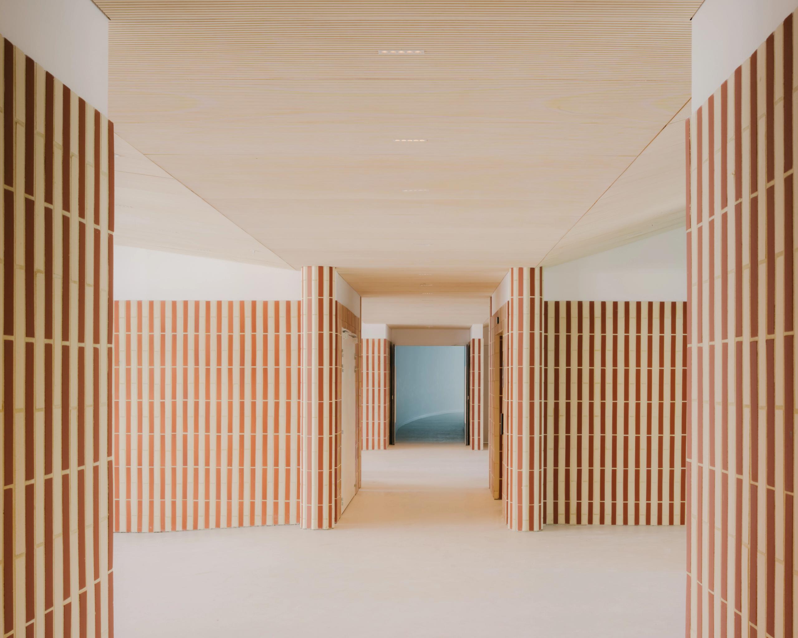 Couloir du groupe scolaire Dominique Frelaut à Colombes, rythmé par des parois en briques de terre cuite et plafond bois, cadrant une perspective vers la cour.