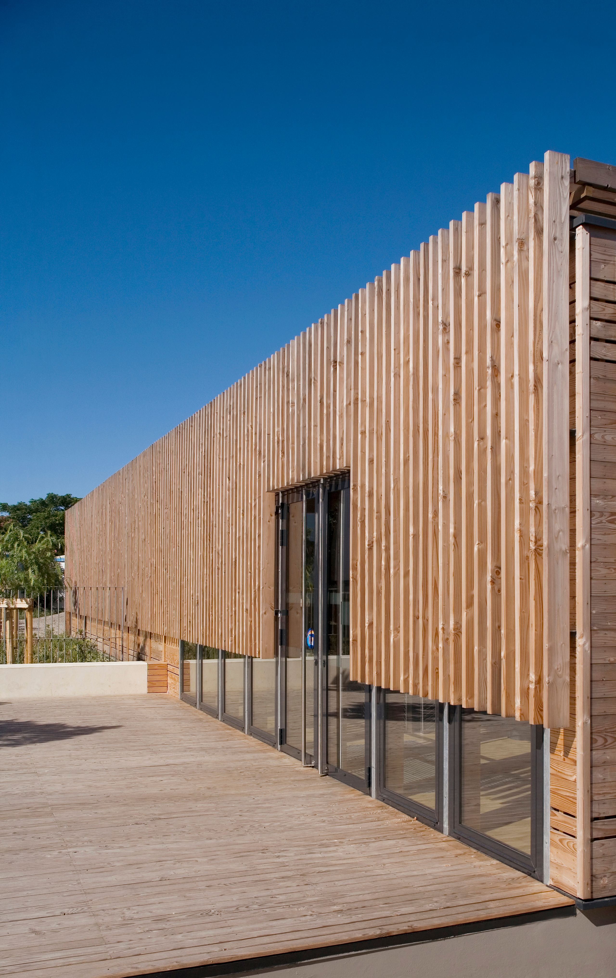 Façade en bois à claire-voie du centre thermal de Balaruc-les-Bains, posée sur un socle vitré et une terrasse en bois, soulignant l’horizontalité du volume.