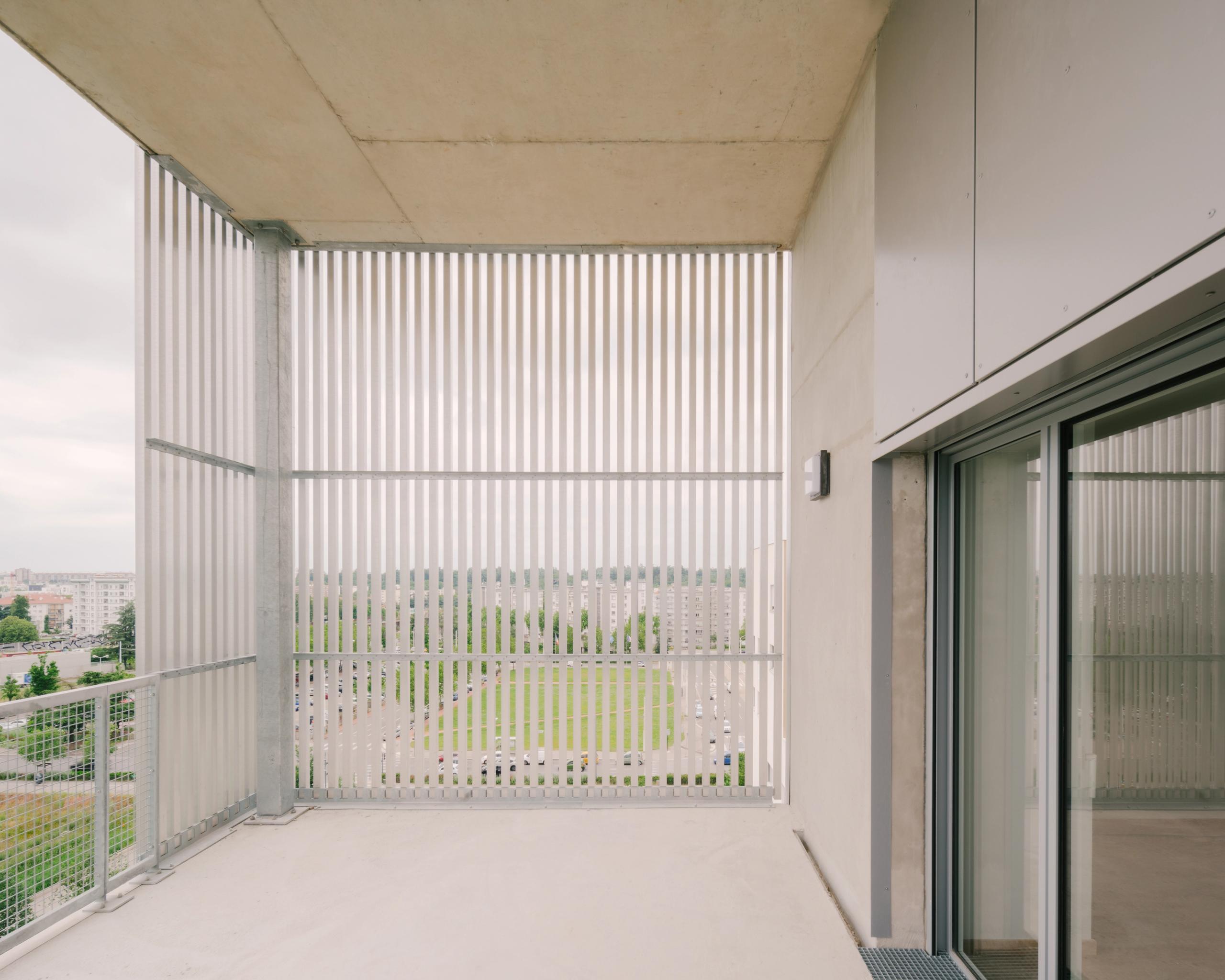 Loggia des 116 logements à Vénissieux par Tectoniques, balcon en exosquelette métallique avec lames verticales filtrant la vue sur le parc urbain.
