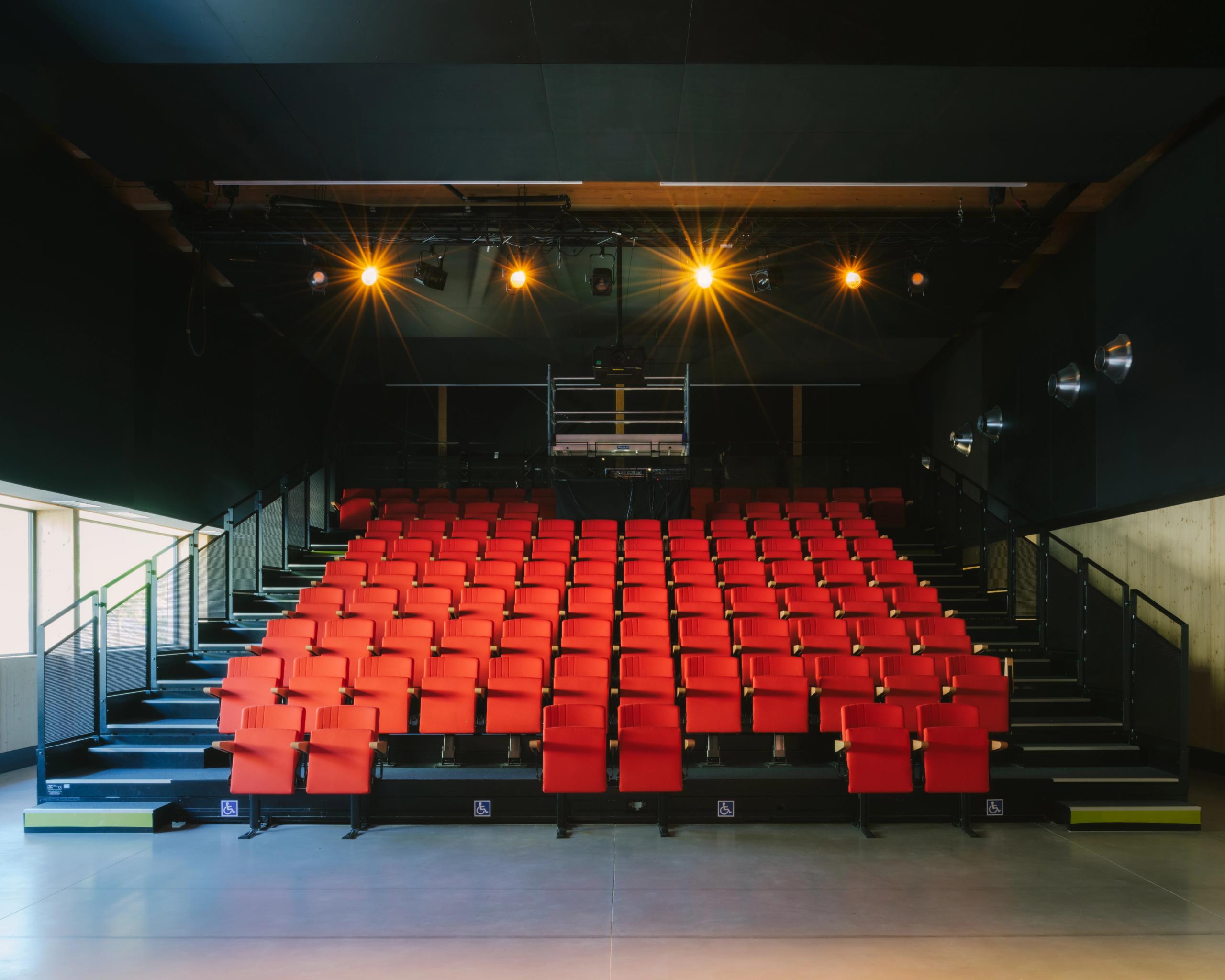 Salle de spectacle de la médiathèque et School complex Claudie Haigneré aux Pennes-Mirabeau, gradins rouges modulaires et boîtes techniques noires.