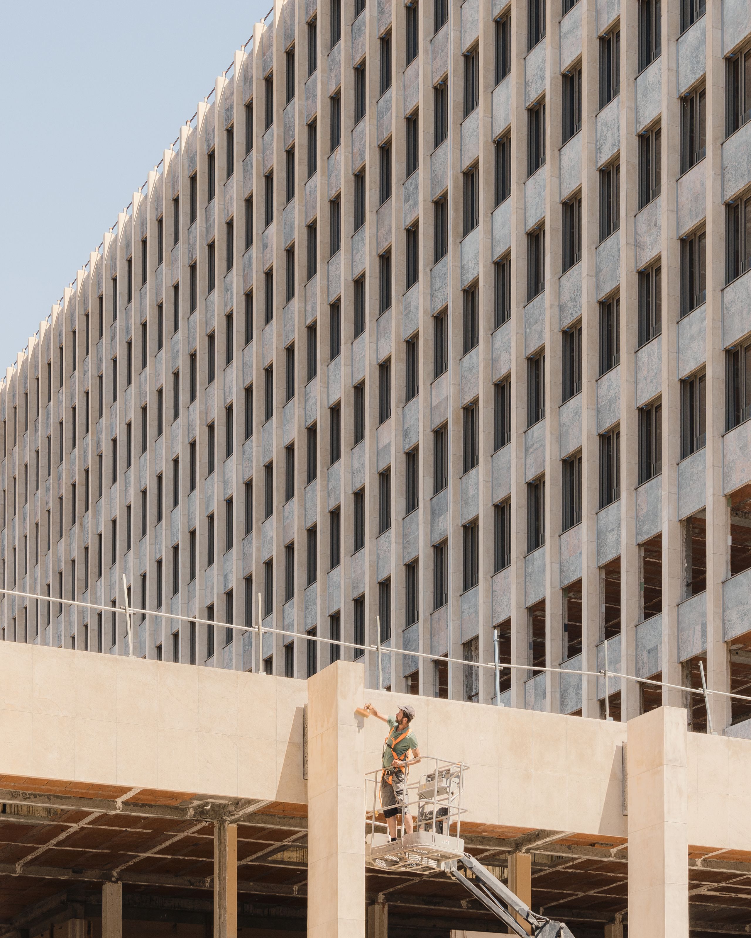 Chantier de réhabilitation de l’IGH Émile Loubet à Saint-Étienne, façade administrative des années 1970 en trame régulière, socle béton en cours de reprise.