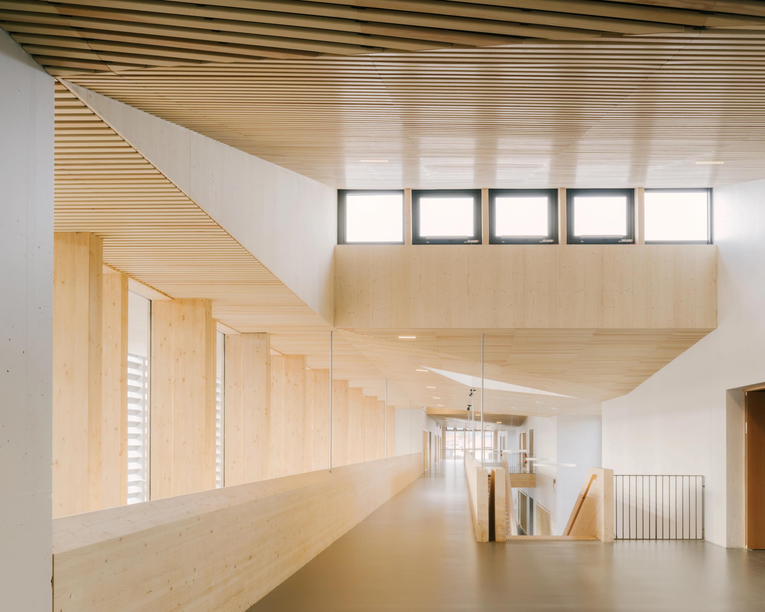 Rue intérieure du Collège du Ban à Vagney, en structure bois vosgien apparente, éclairée par des baies hautes et ouvrant sur les circulations et le préau.
