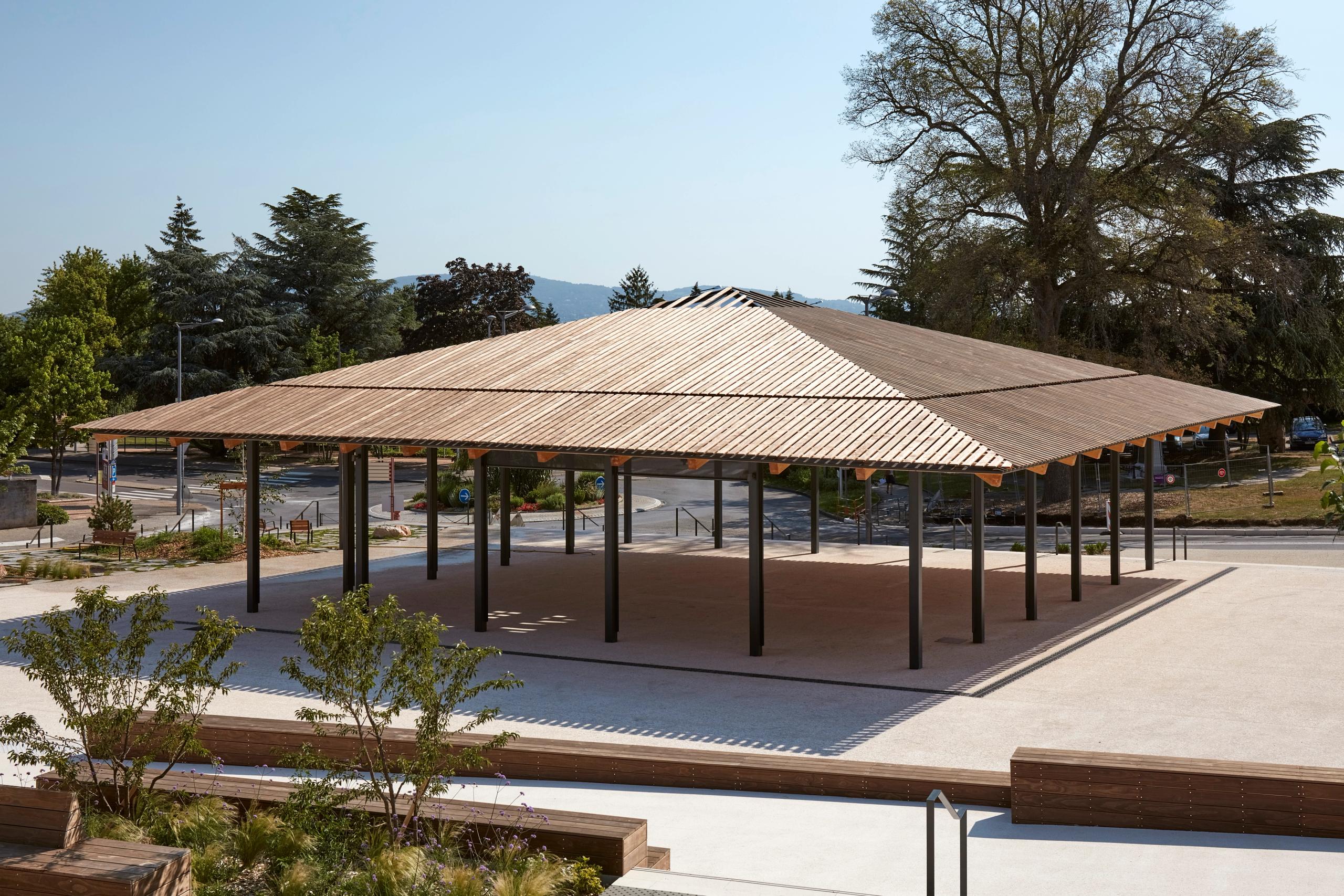 Halle de marché de Marcy-l’Étoile par Tectoniques : vaste toiture carrée en bois sur poteaux métalliques noirs, couvrant un espace public minéral ouvert.