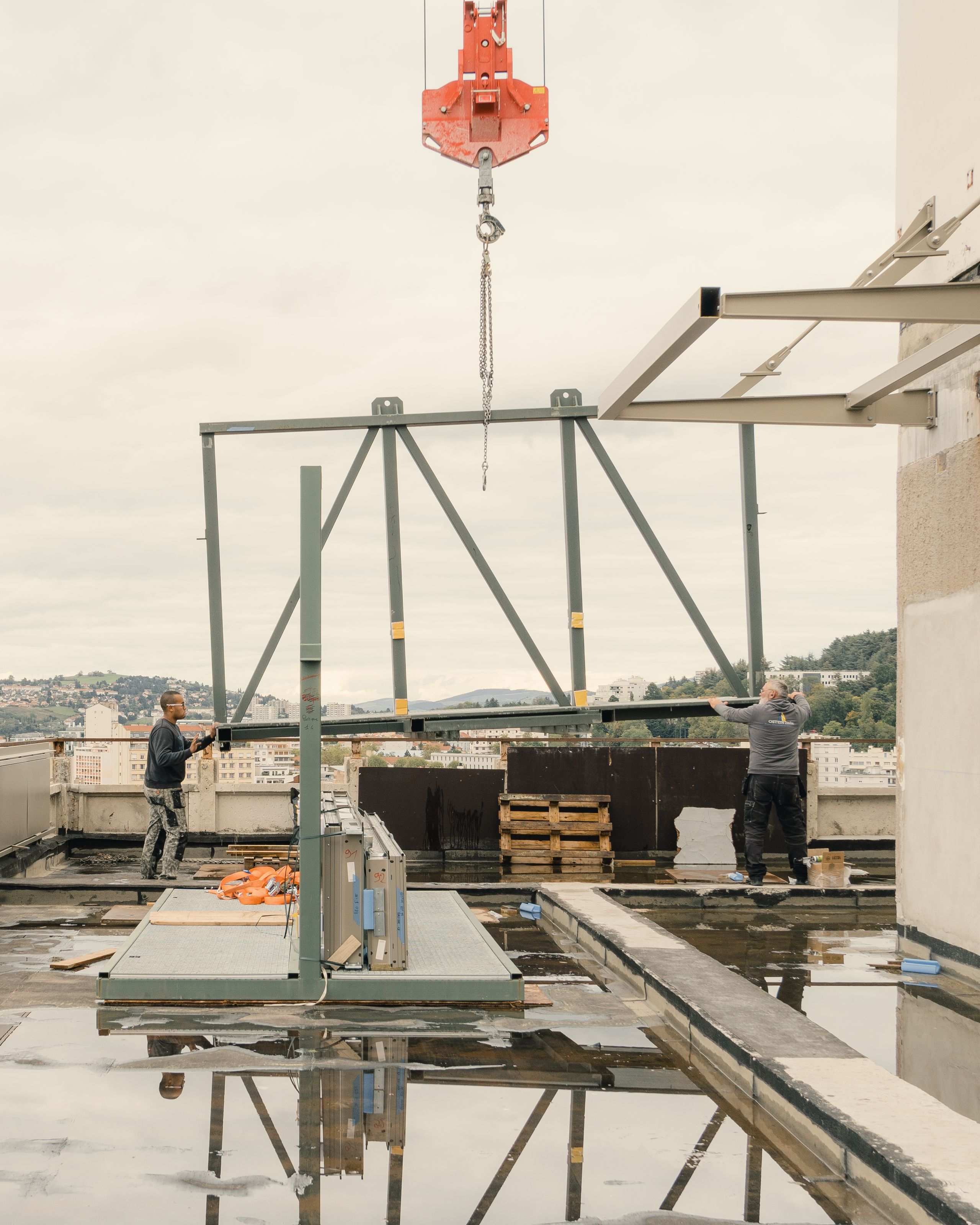 Chantier de réhabilitation de l’IGH Émile Loubet à Saint-Étienne, pose d’une ossature métallique en toiture-terrasse avec grue et vue sur le tissu urbain.