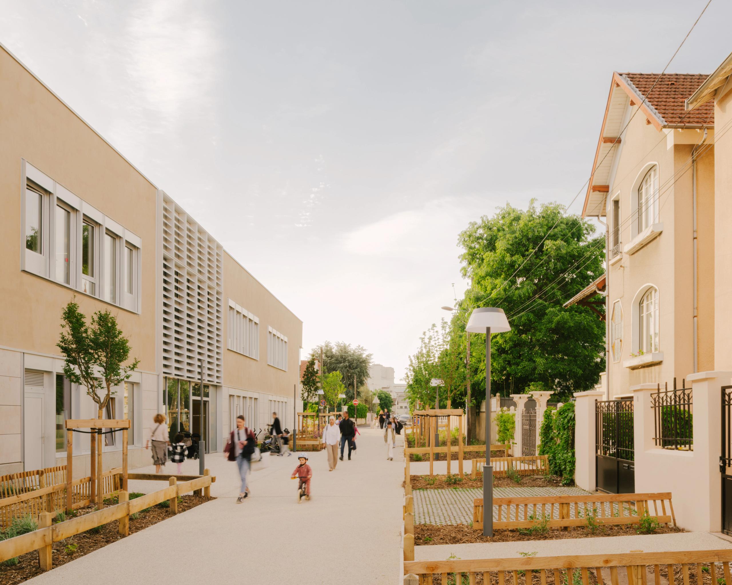 Façade minérale du groupe scolaire Kennedy à Lyon, volume simple en équerre, brise-soleil verticaux, cour plantée et cheminement piéton animé en premier plan.