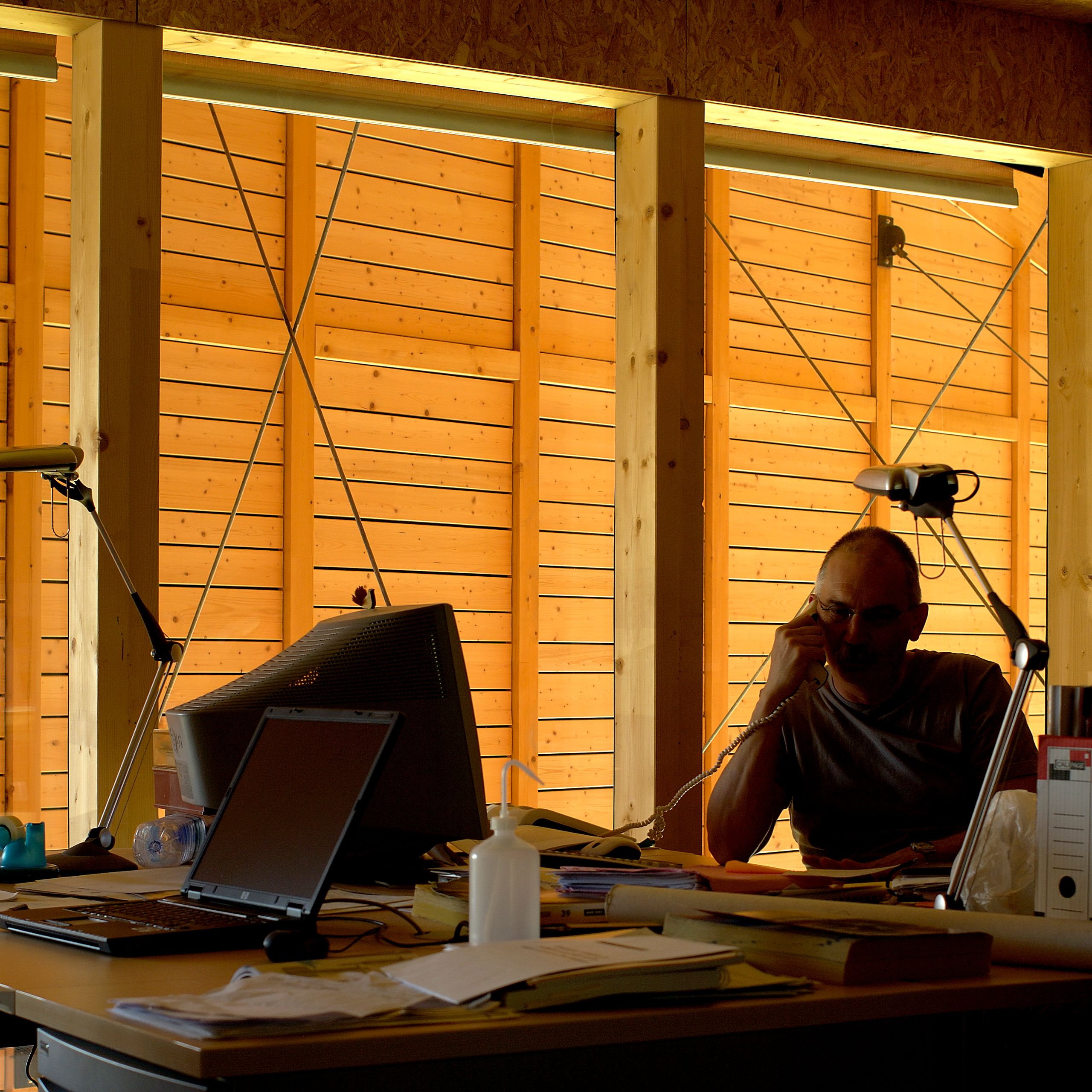 Intérieur de la Maison du Parc du Haut-Jura à Lajoux, bureau devant paroi en ossature bois et bardage intérieur éclairé, montrant la double peau thermique.