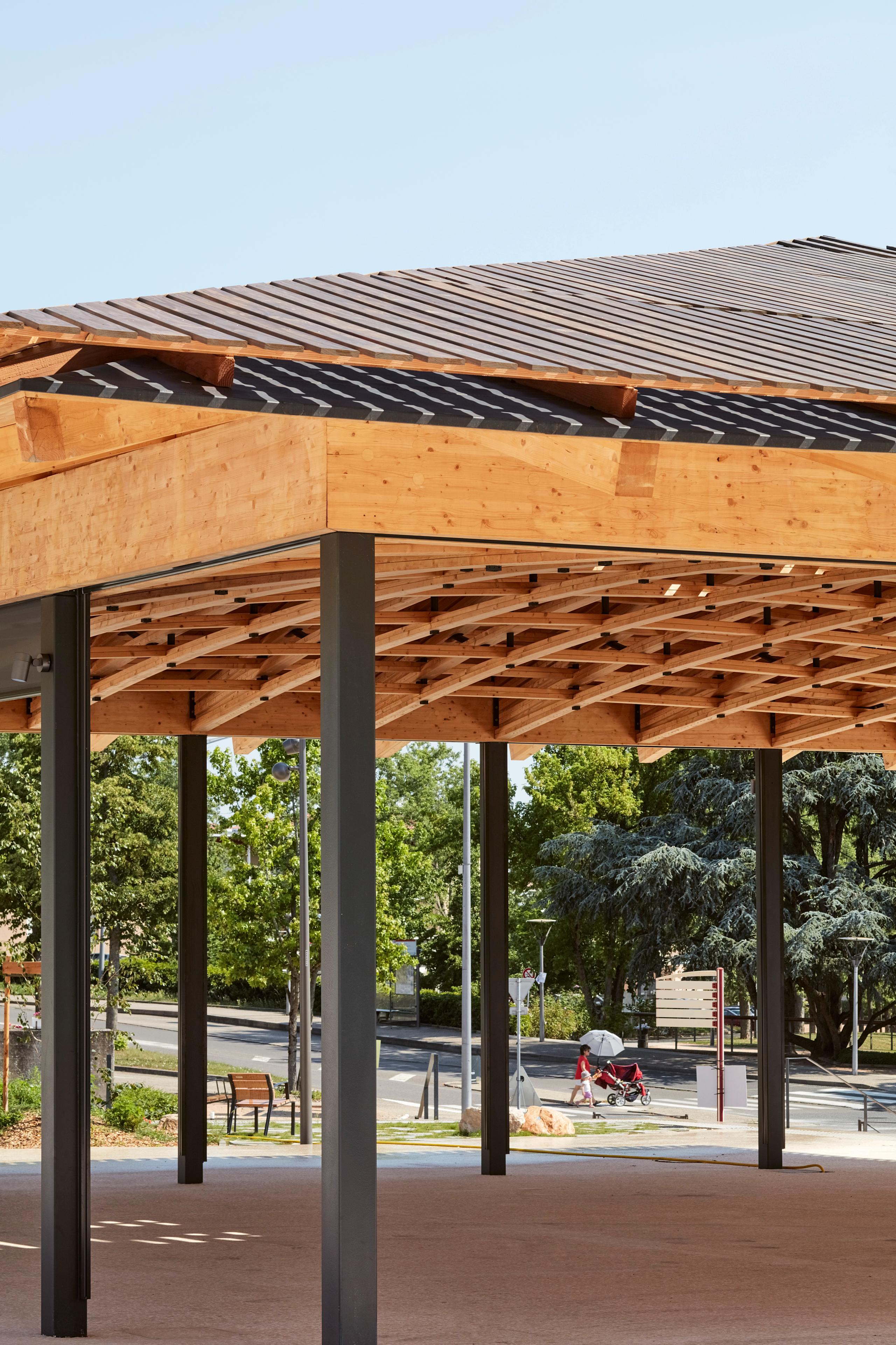 Halle de marché à Marcy-l’Étoile : toiture à quatre pans en bois lamellé-collé, treillis tridimensionnel apparent, portée sur poteaux métalliques noirs.