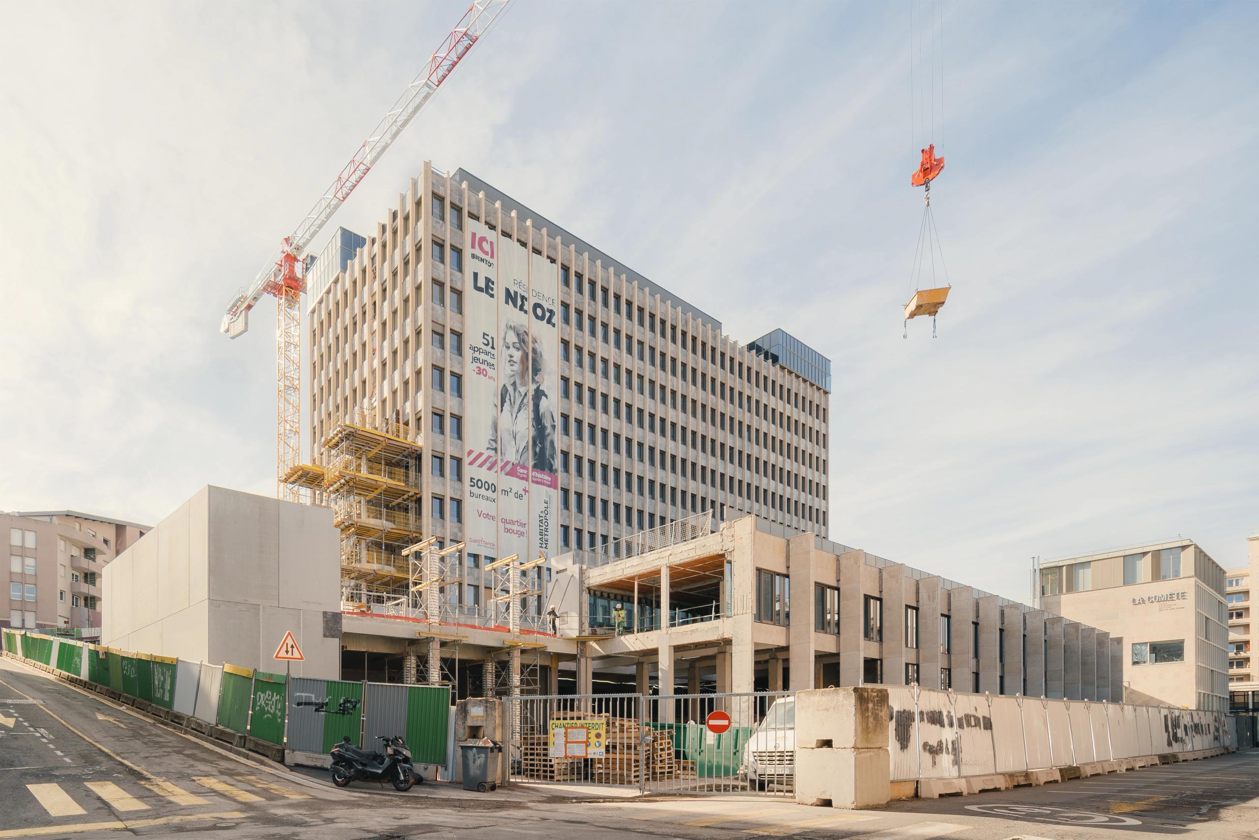 Chantier de réhabilitation de l’IGH Émile Loubet à Saint-Étienne, montrant le socle ouvert, la tour restaurée, les échafaudages et la grue en activité.
