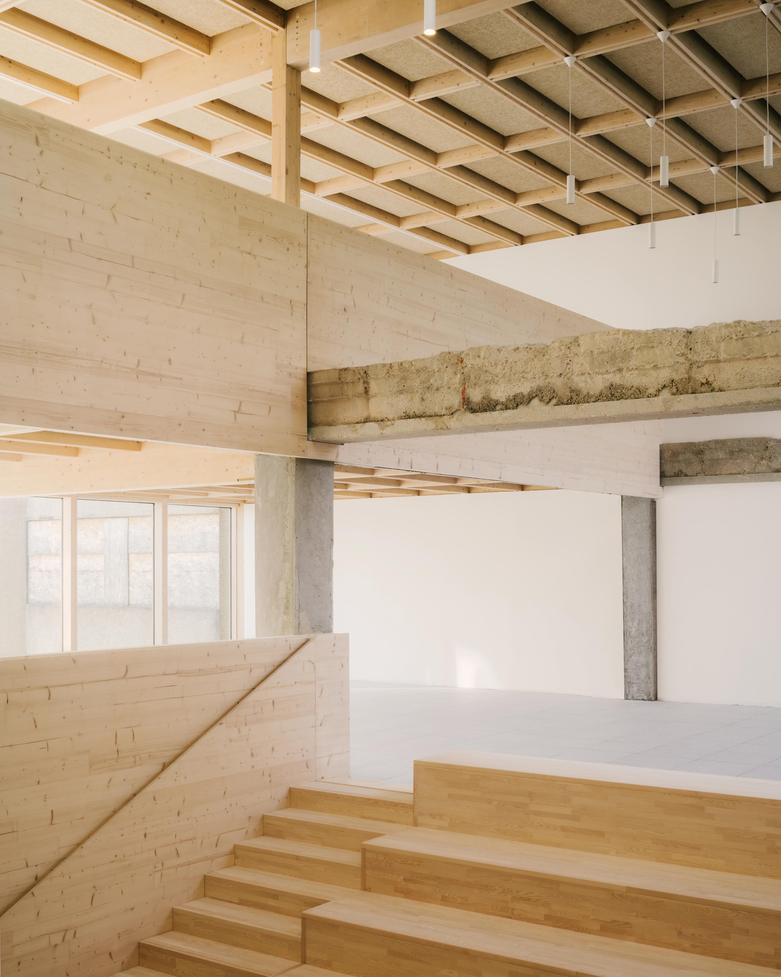 Intérieur du collège Maryse Bastié à Dole : gradins en bois, structure mixte béton/bois apparente et plafond caisson, illustrant la Restructuration.