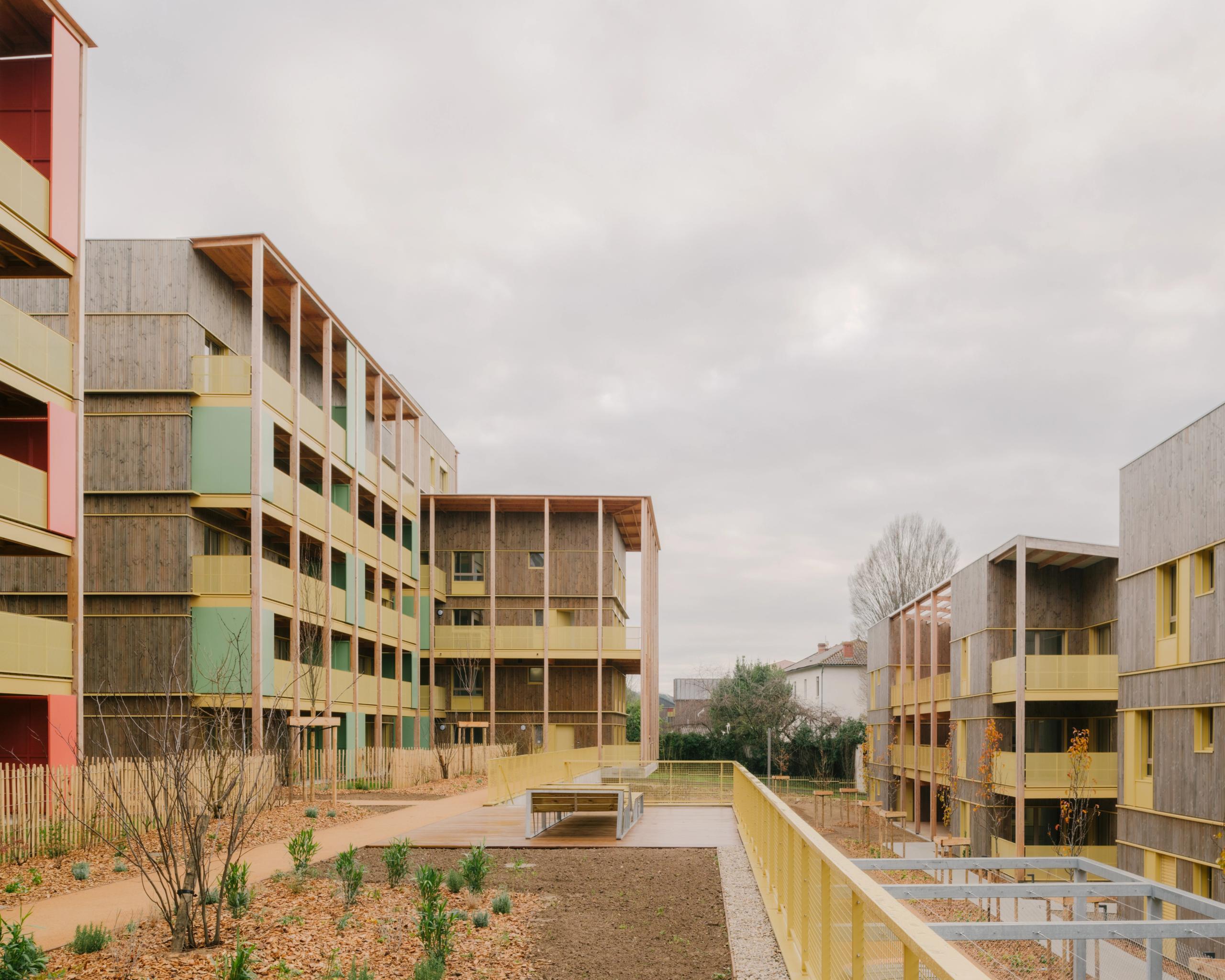 Vue des 84 logements à Trévoux par Tectoniques : volumes en gradins, structure bois-béton, coursives extérieures colorées et grands balcons sur parc public.