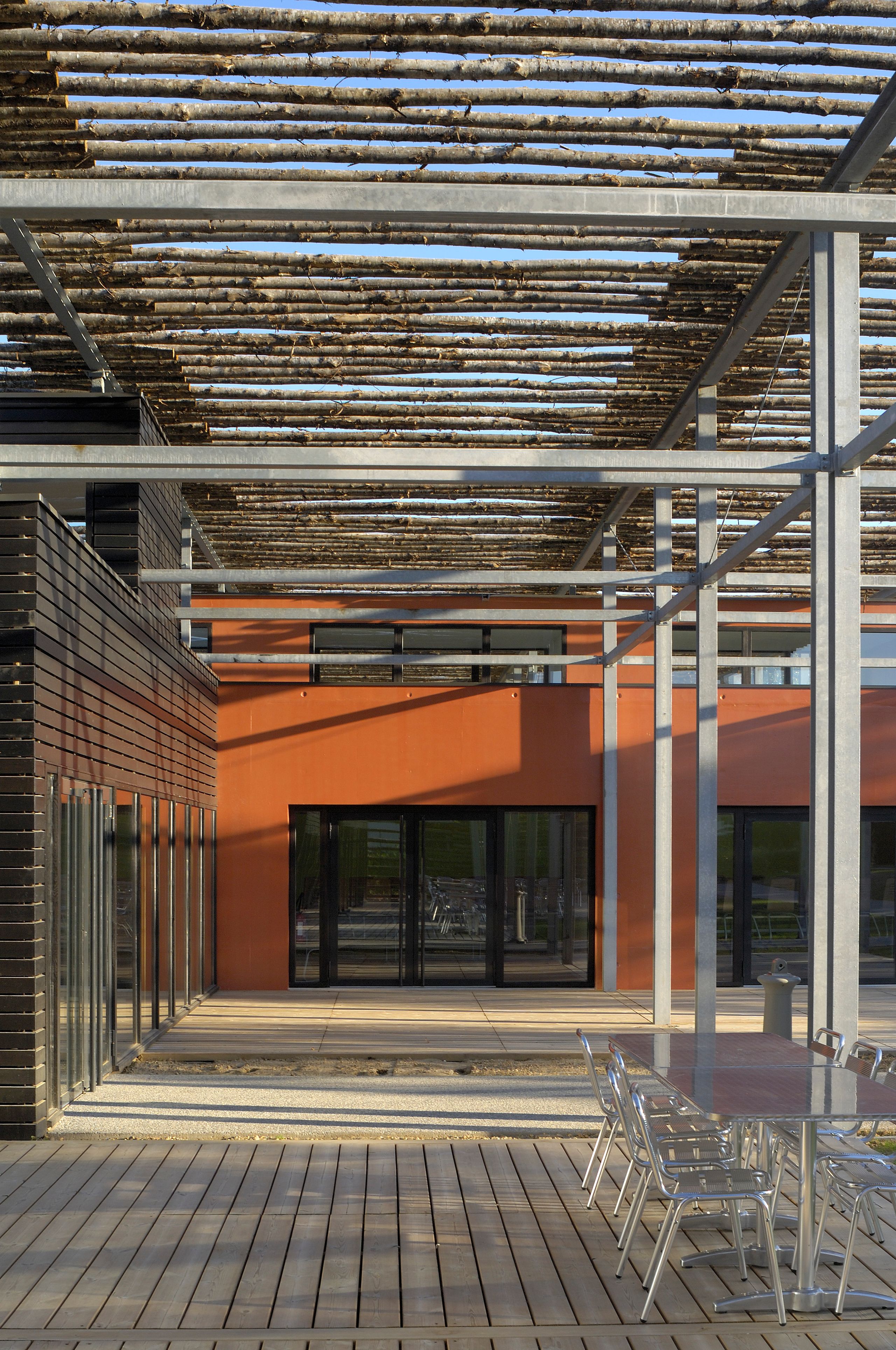 Terrasse du restaurant administratif du CETE à Bron, sous ombrière en baliveaux de châtaignier sur exostructure métallique, ouvrant sur les volumes vitrés.