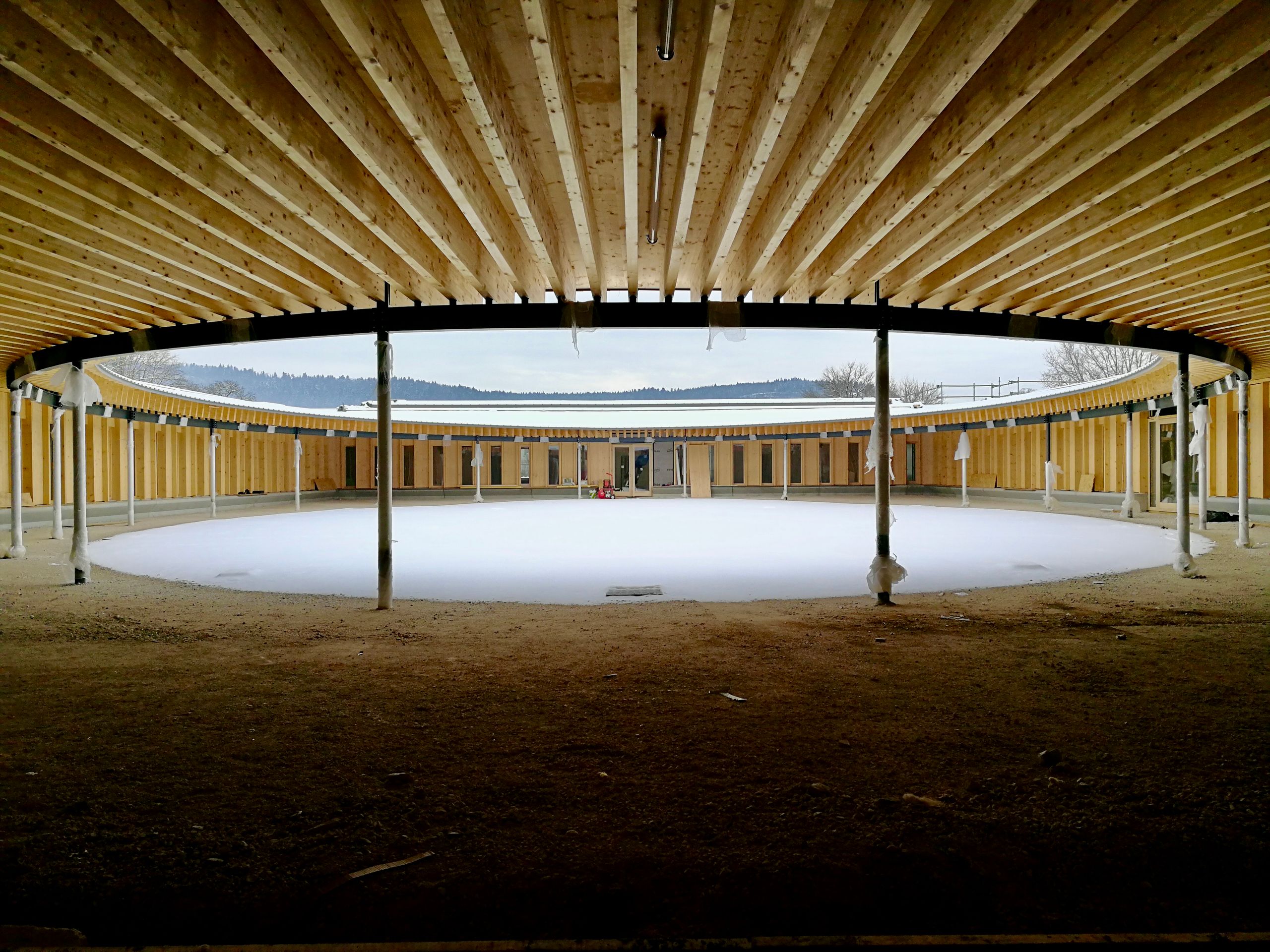 Cour elliptique de l’école élémentaire Hubert Reeves à Champagnole, couverte par une toiture en impluvium en bois du Jura, ouverte sur le paysage lointain.