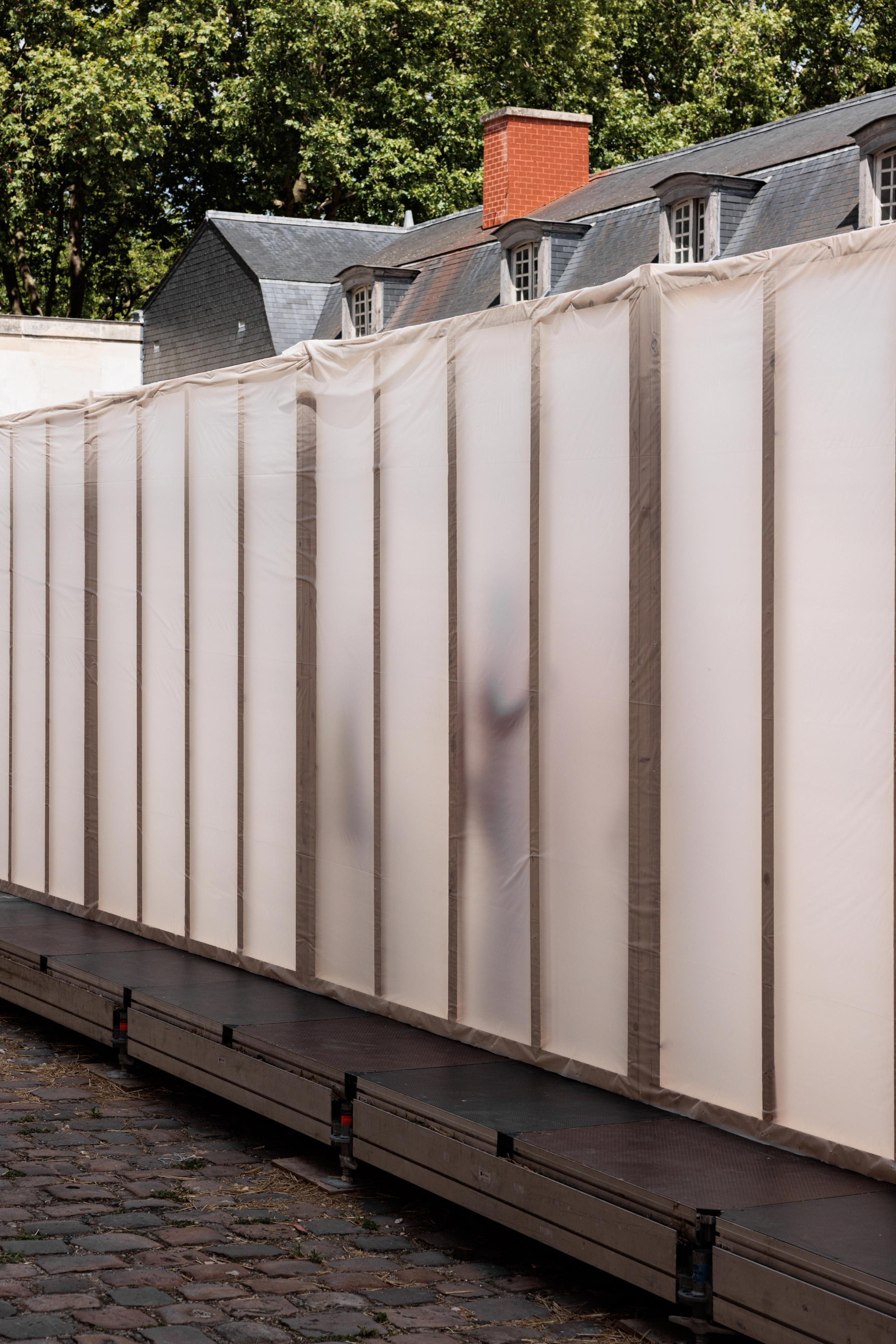 Workshop 60x60 à Versailles : paroi longitudinale en ossature bois et film plastique translucide, posée sur platelage modulaire dans la cour pavée.