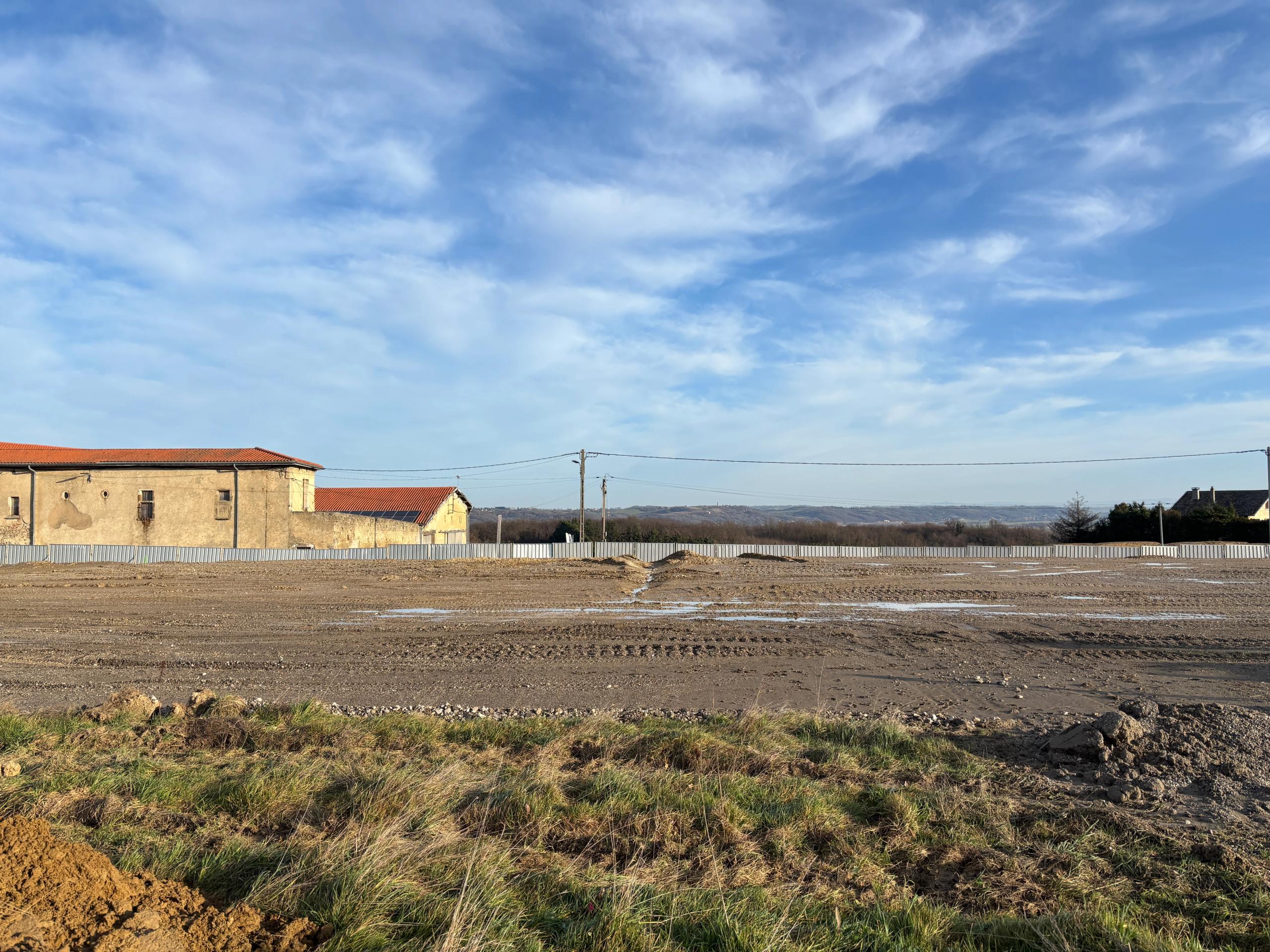 Terrassements du futur groupe scolaire de Vienne : merlons de terre géométriques implantés sur le versant, ouverts sur le paysage lointain en belvédère.