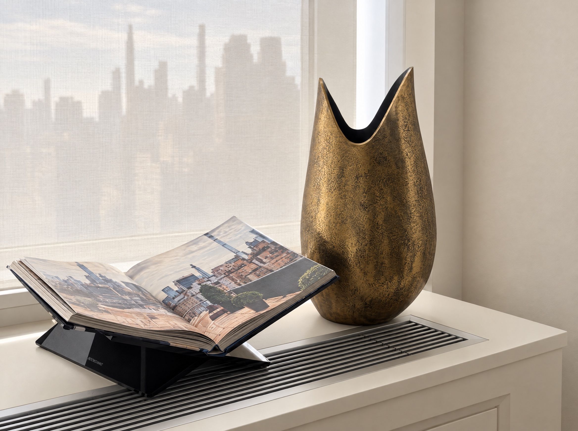 Hammered brass vase and an open book of Manhattan photographs on a white radiator cabinet by the window