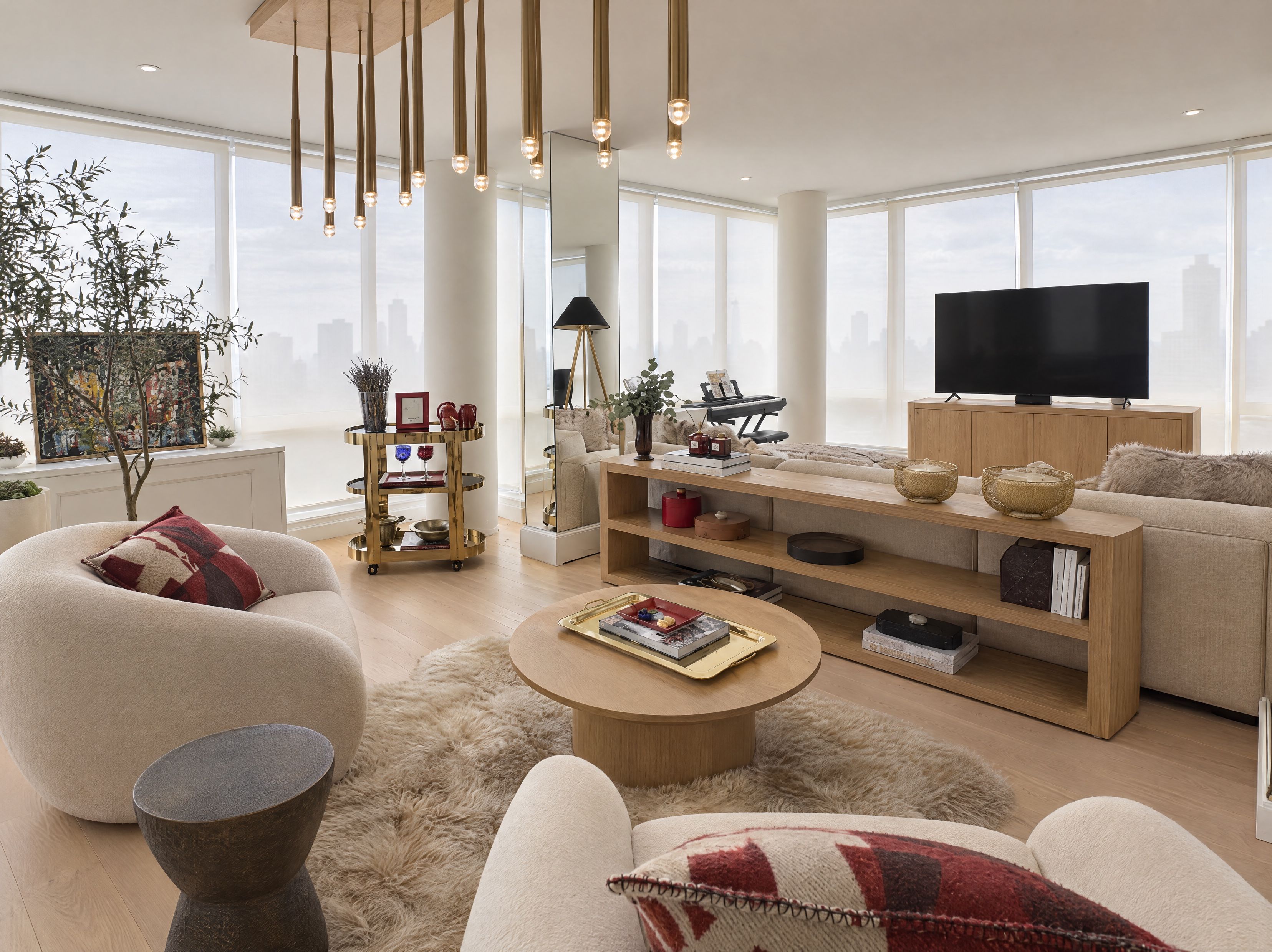 Living room seating area with a cluster of brass pendant lights, cream boucle armchairs and a sheepskin rug, Upper East Side apartment