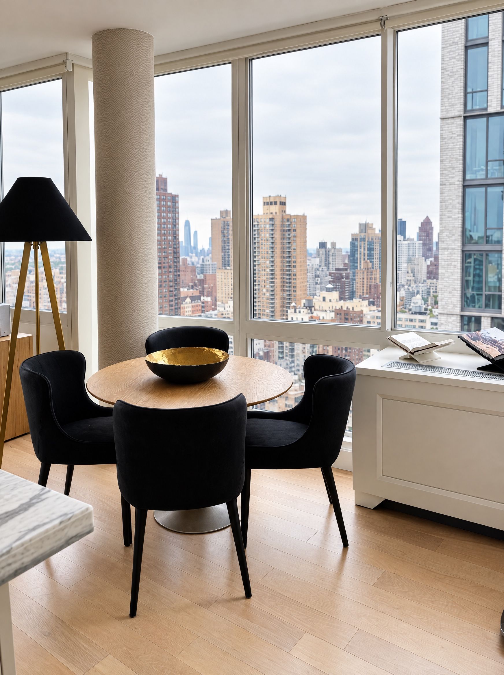 Round oak dining table with four black velvet chairs against floor-to-ceiling windows and the Manhattan skyline