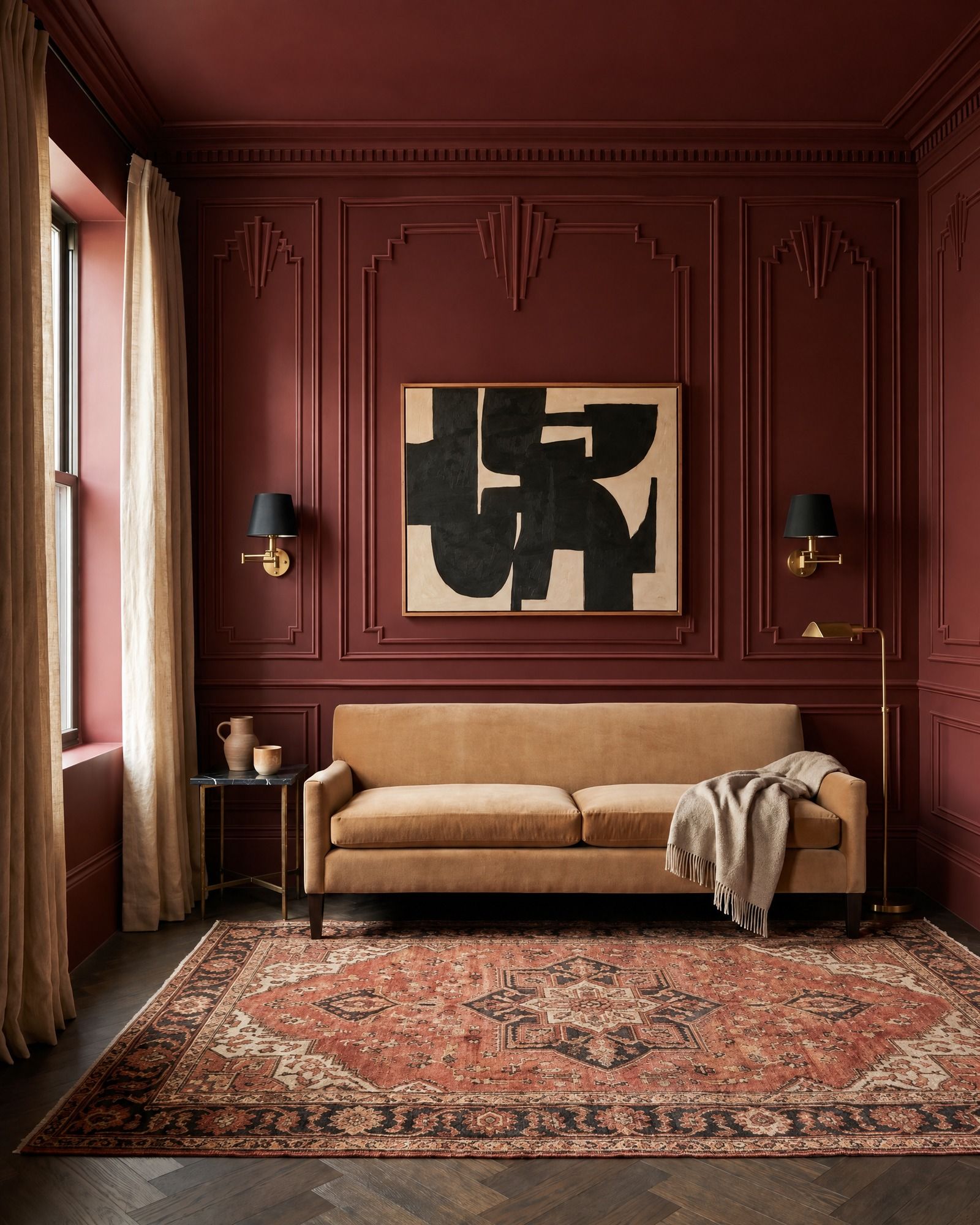 An oxblood sitting room with a camel velvet sofa and a black-and-cream painting, tall double-line panels of molding whose tops step up into Art Deco fans, laid out around the painting and the black-shaded sconces, with a stepped crown above