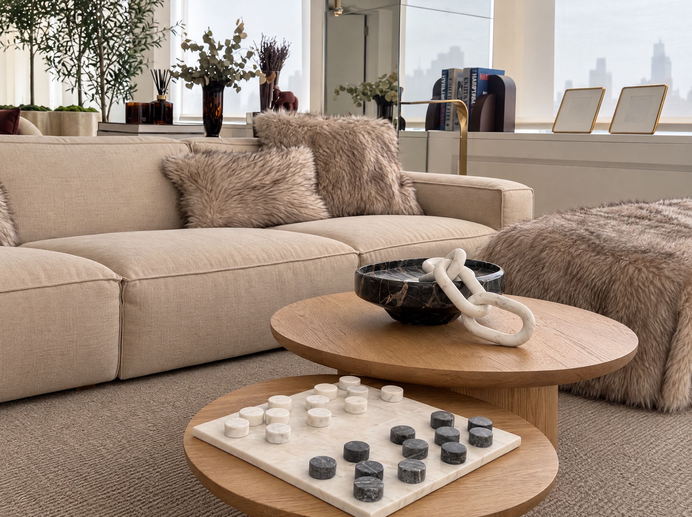Nesting oak coffee tables with a marble checkers set and a marble chain sculpture in front of a linen sofa