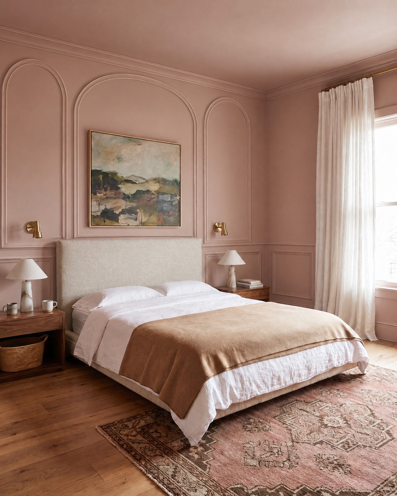 A plaster-pink bedroom with a linen headboard and a landscape painting, three tall arched panels of molding on the wall, the widest around the painting over the bed, with a crown above