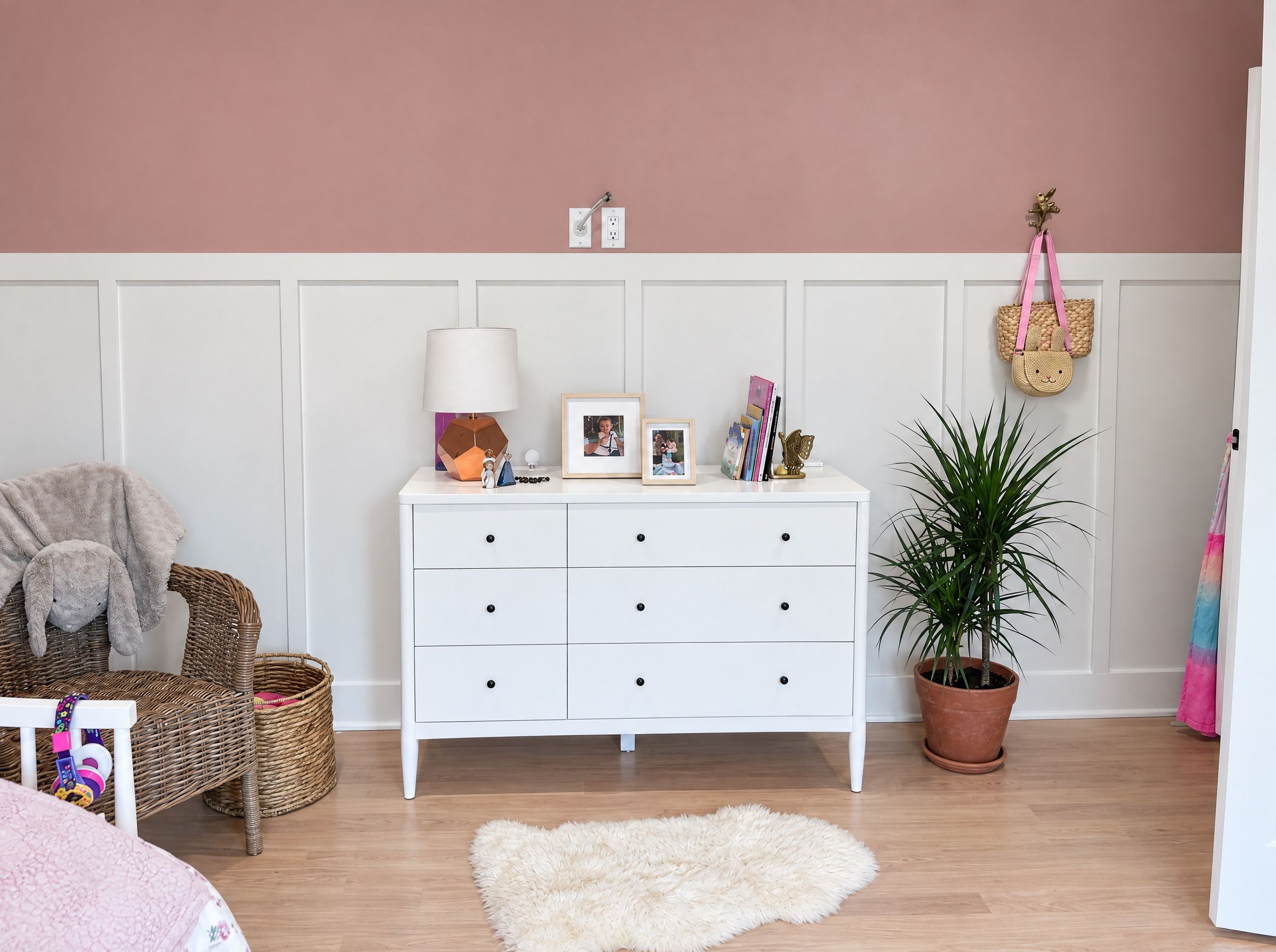 A white dresser with a lamp and framed photos against the girls' room wainscoting