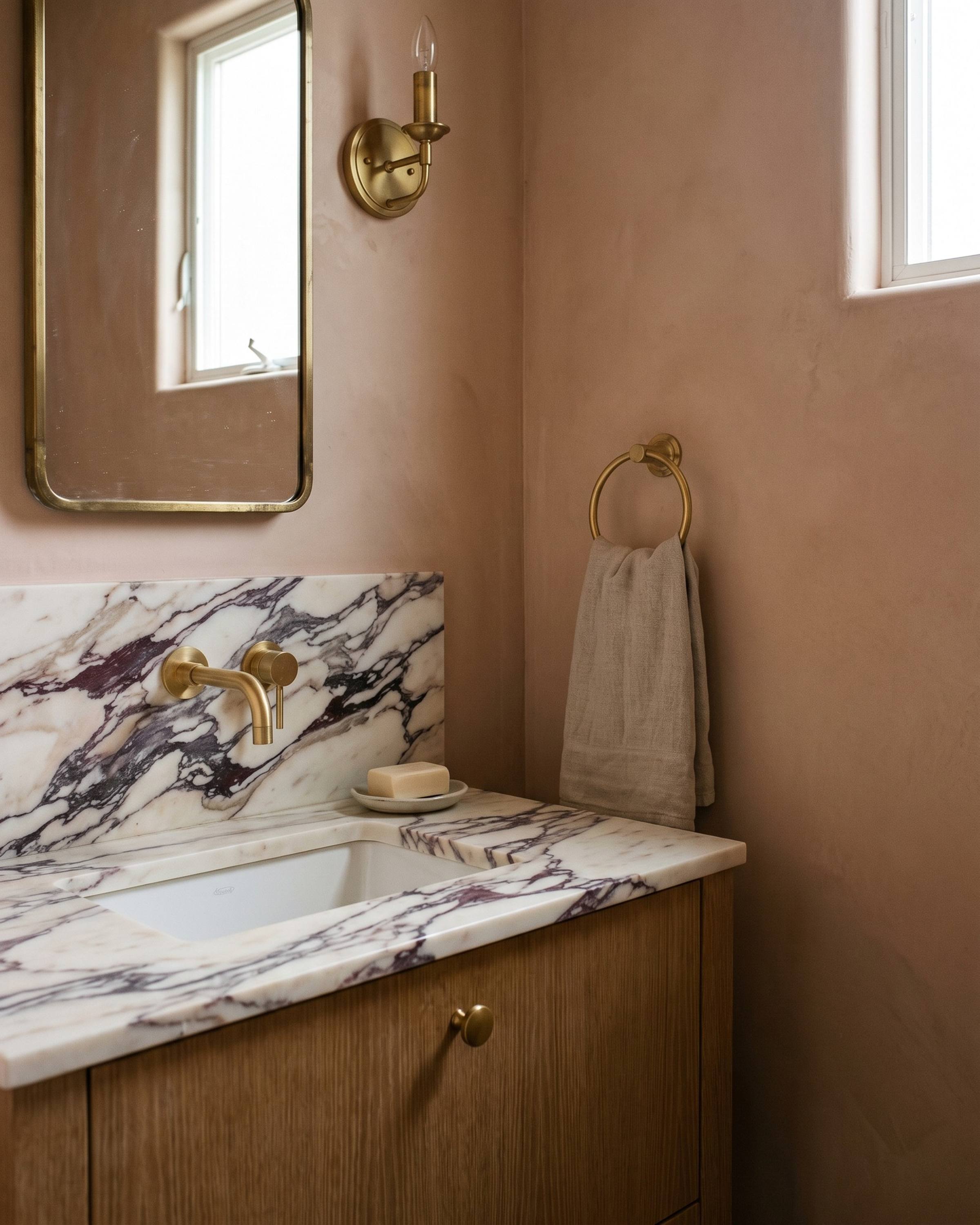 A powder room vanity in honed Calacatta Viola marble, burgundy and violet veins on cream, on a rift oak base against clay-pink plaster