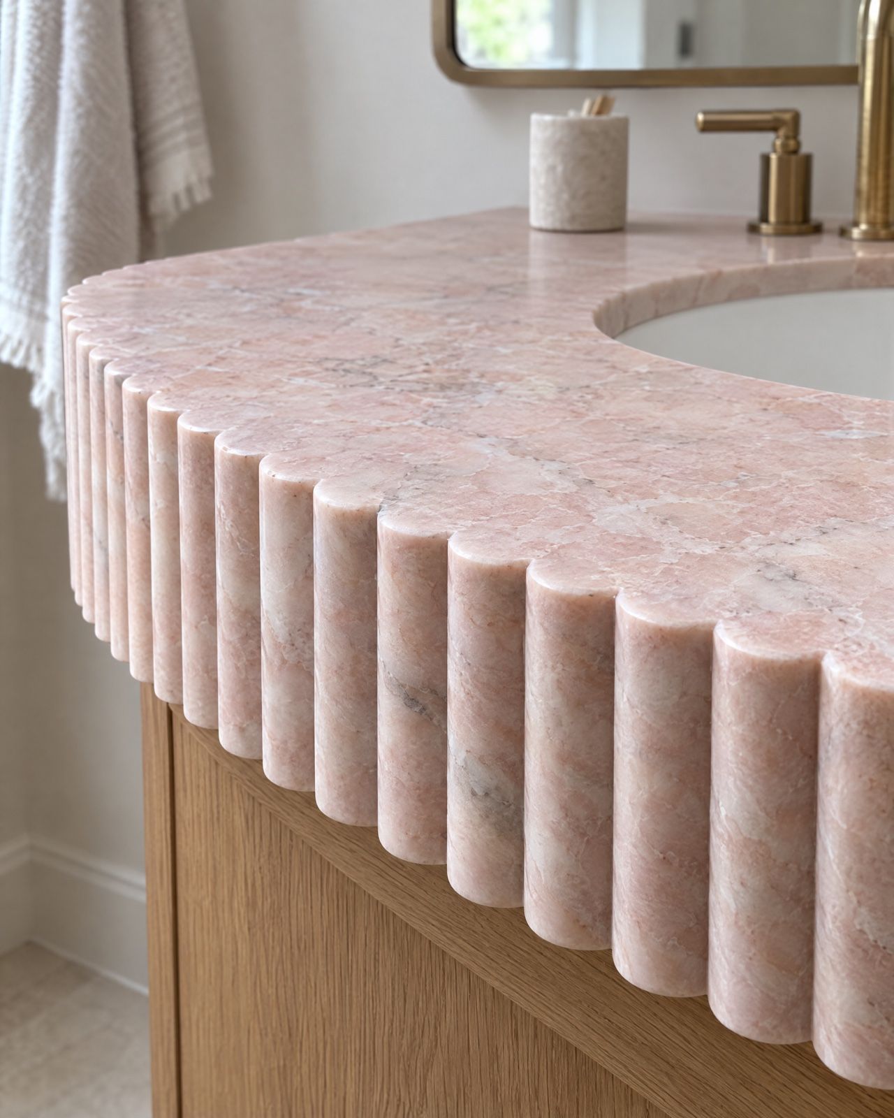 A curved pink marble vanity top whose thick edge is carved into vertical rounded ribs