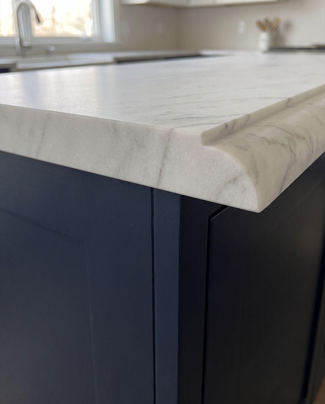 The cut end of a white marble countertop showing a Dupont edge in section: a square step, then a large quarter-round