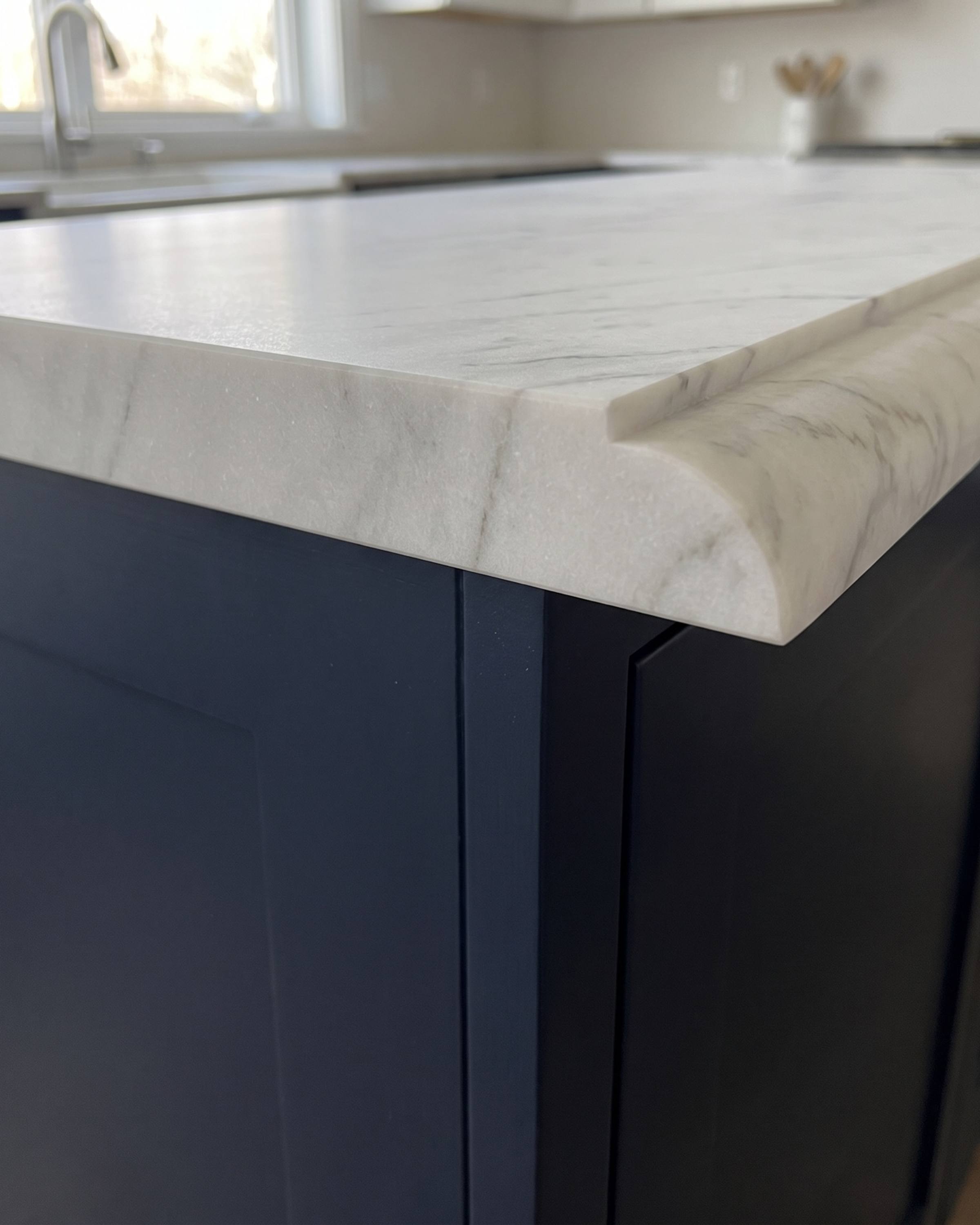 The cut end of a white marble countertop showing a Dupont edge in section: a square step, then a large quarter-round