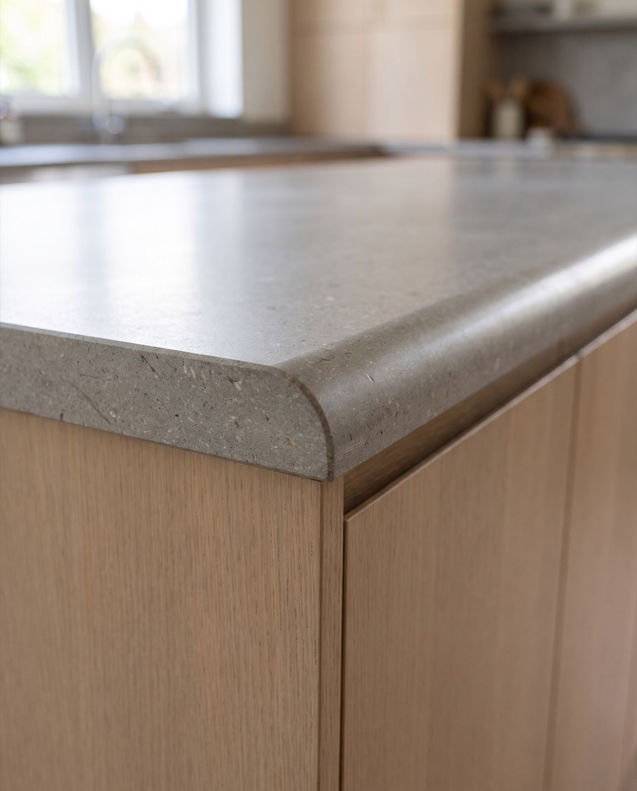 The cut end of a grey limestone countertop showing a half bullnose edge in section: rounded on top, flat underneath