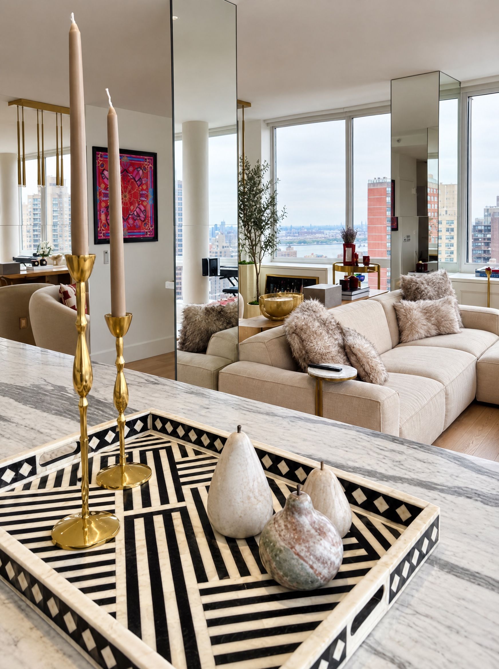 Bone-inlay tray with brass candlesticks on the marble island, the sofa reflected in the mirrored column behind