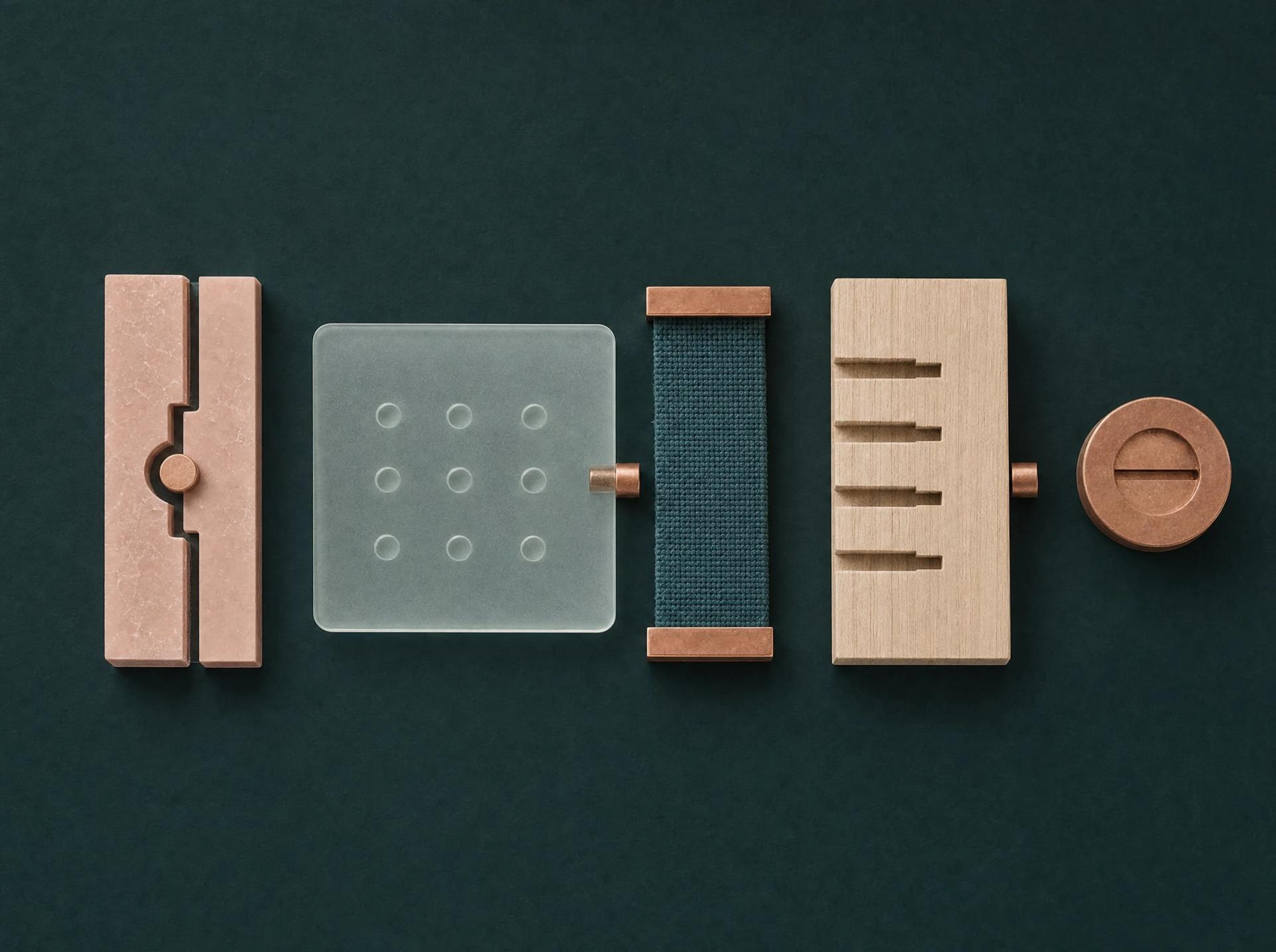 Overhead sequence of blush glass, blue textile, timber and copper components arranged on a forest-green ground.