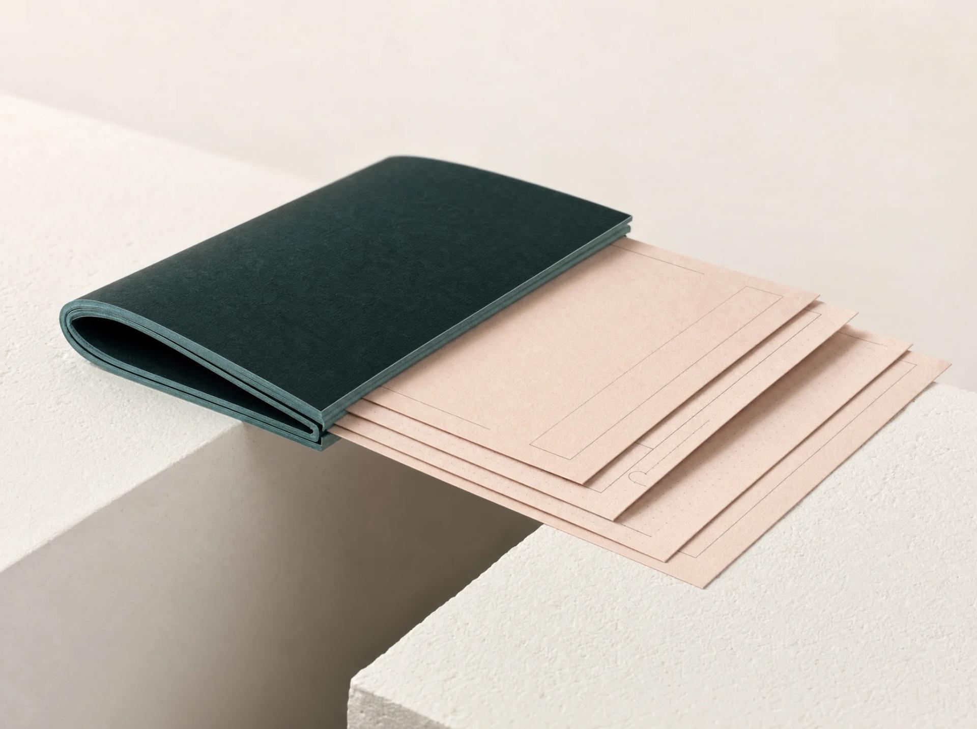 A deep green portfolio holding ordered blush planning sheets above a precise cutout.