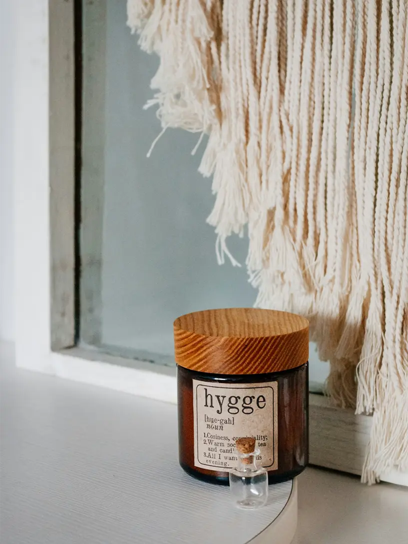 Krukke med hygge-etiket og trælåg foran vindue med makramé-ophæng