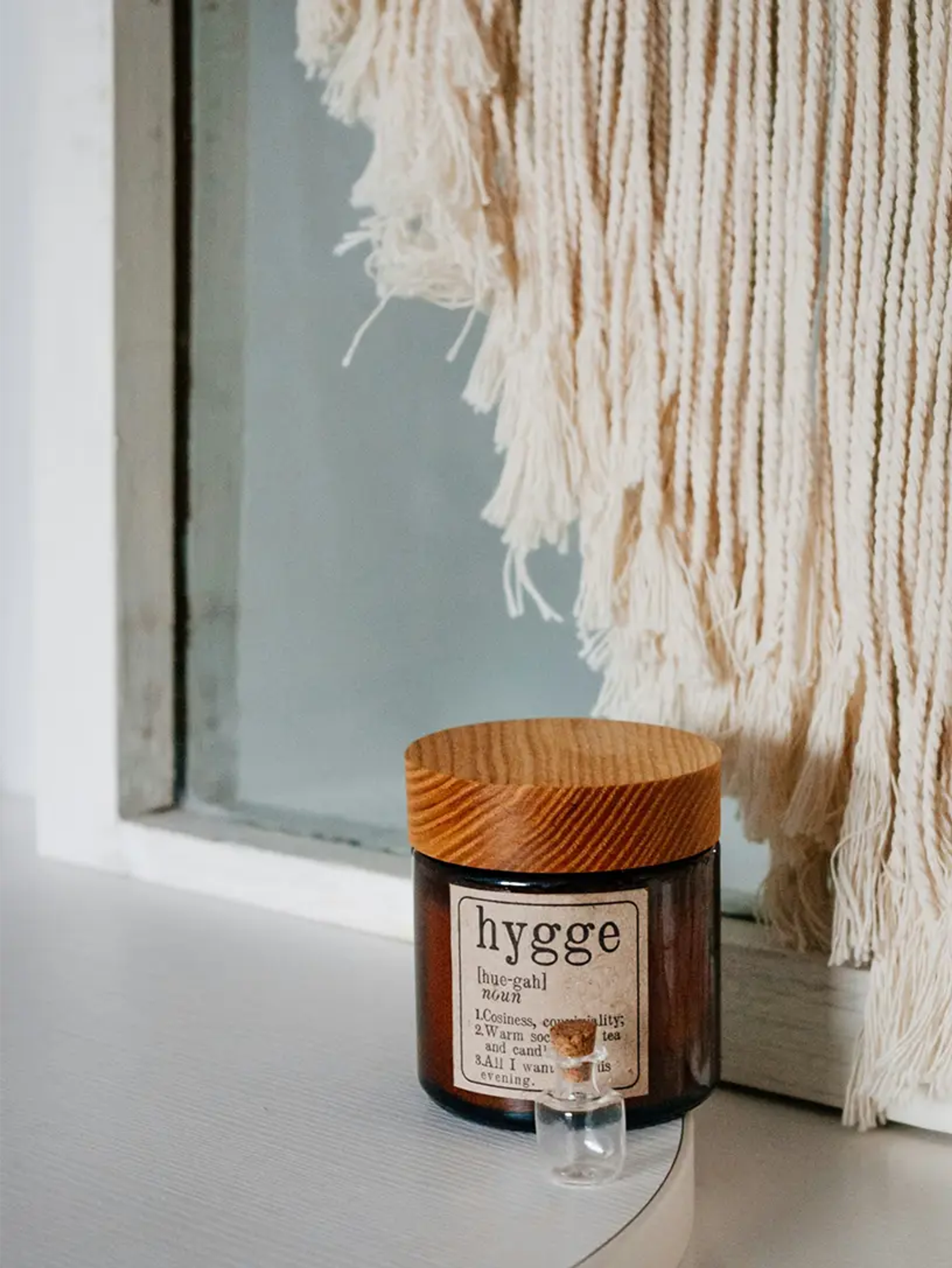 Krukke med hygge-etiket og trælåg foran vindue med makramé-ophæng