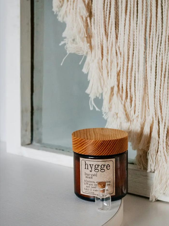 Krukke med hygge-etiket og trælåg foran vindue med makramé-ophæng