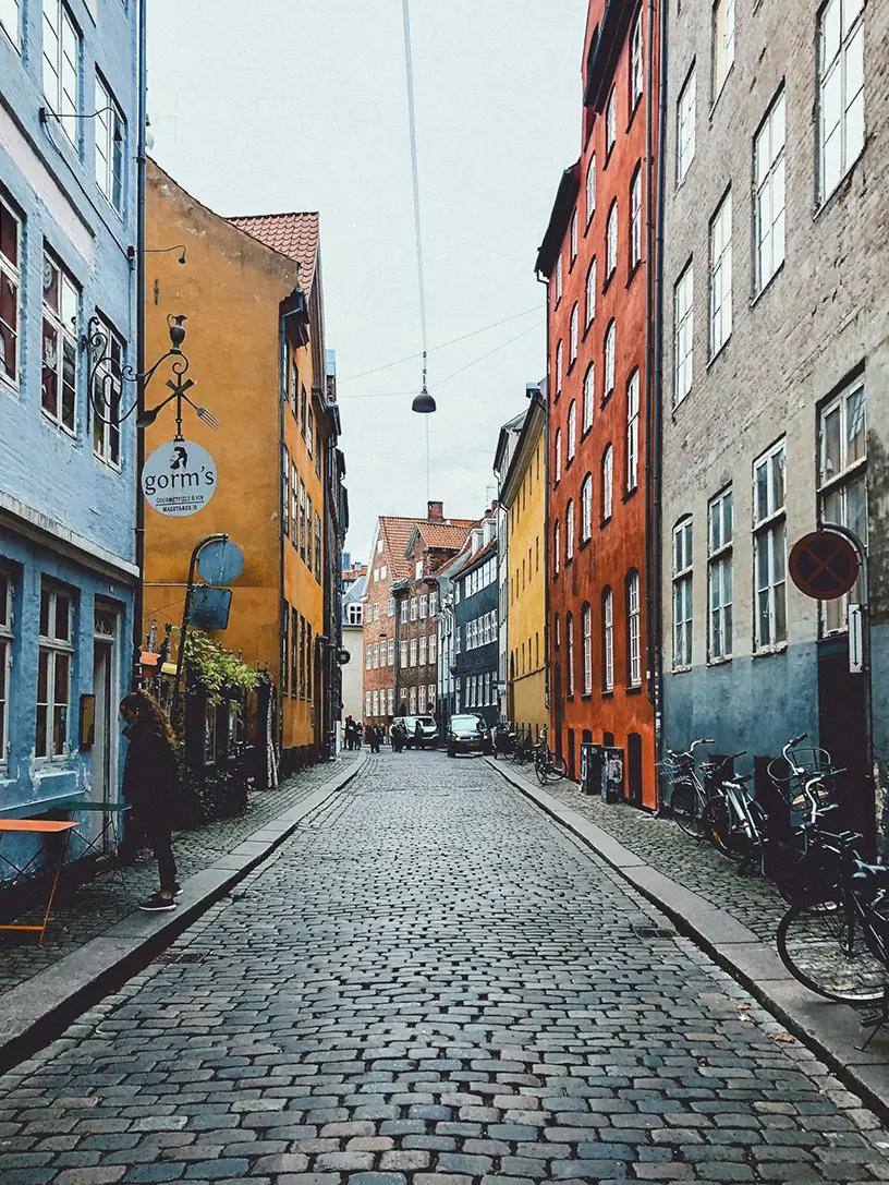 Brostensbelagt gade i København med farverige ejendomme på begge sider.