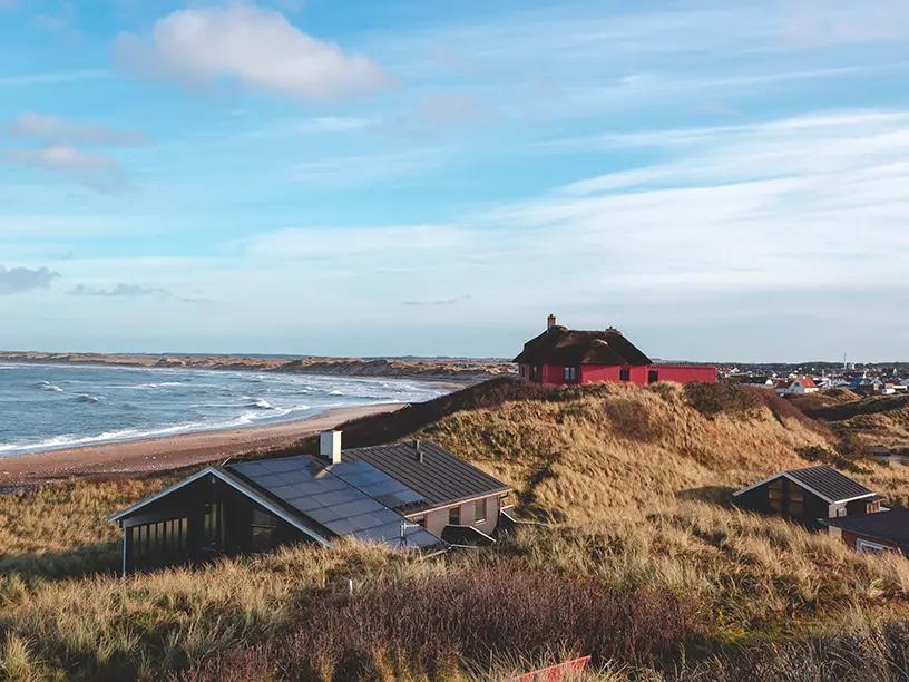 Et rødt hus ligger på toppen af en bakke, med udsigt over havet, med et boliglån.
