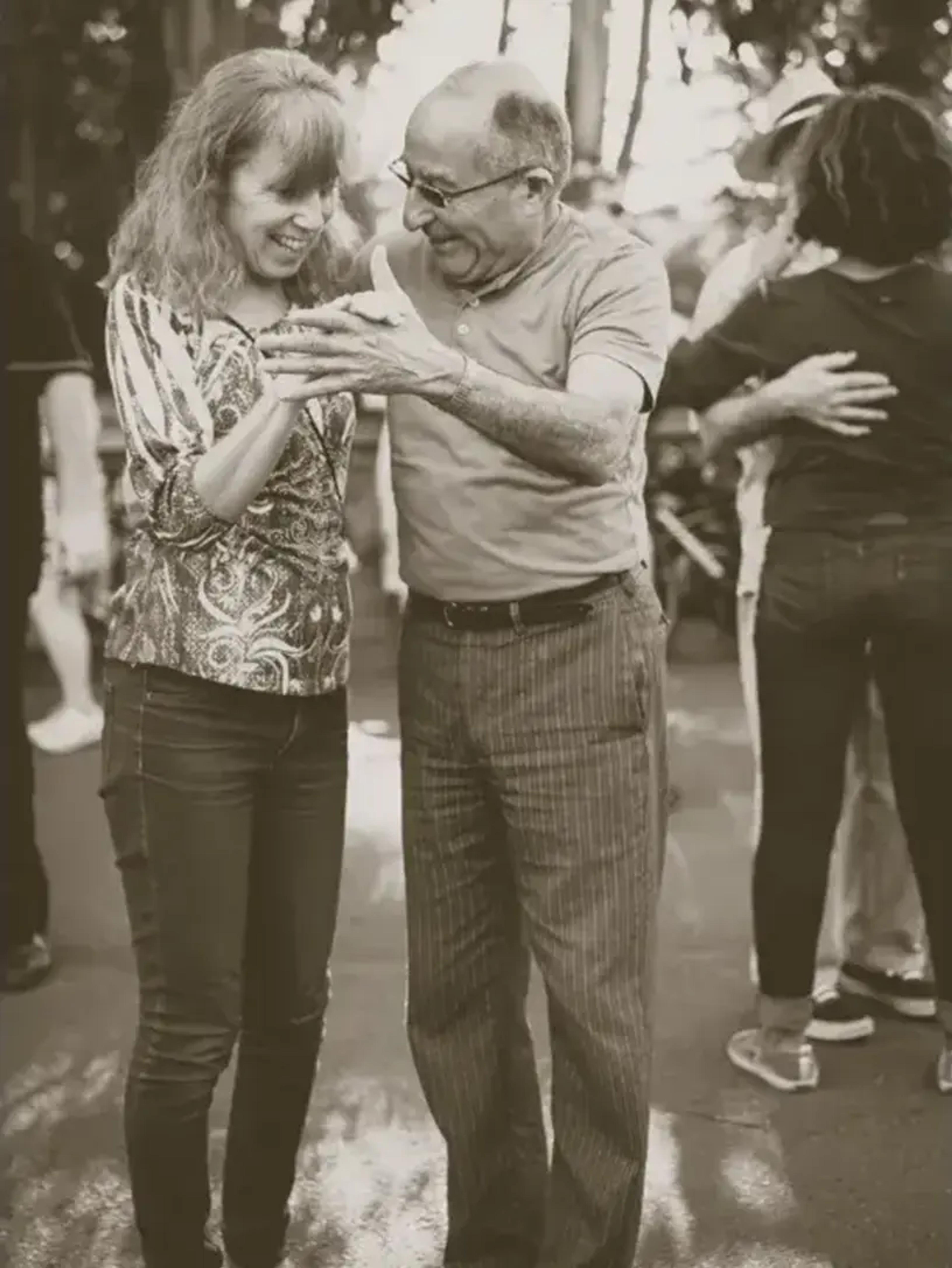 Ældre mand og yngre kvinde danser smilende sammen udendørs.