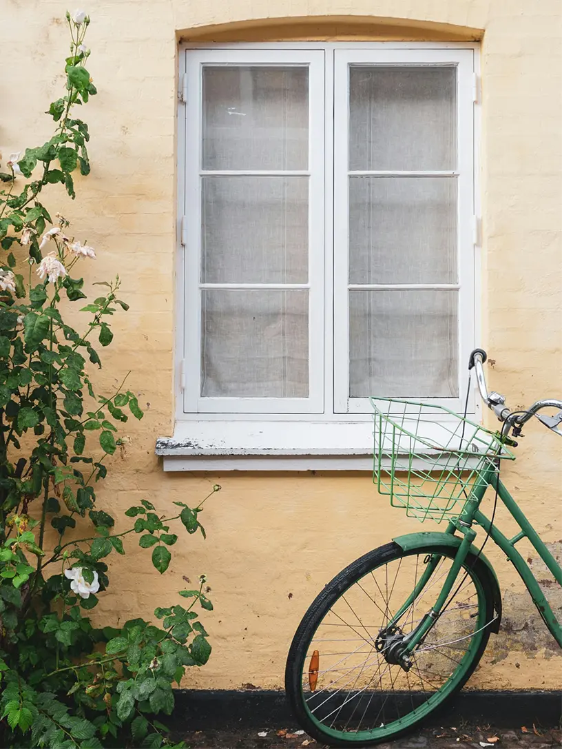 Grøn cykel parkeret op ad gul husmur med vindue og roser