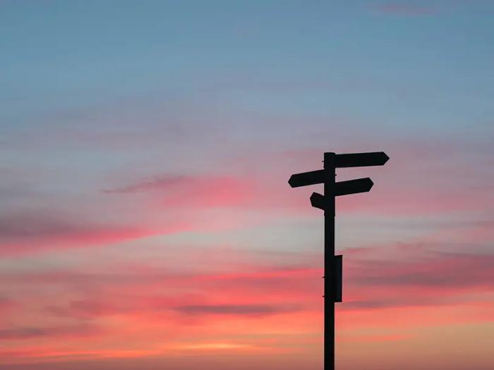 En retningsskilt silhuet ved solnedgang.