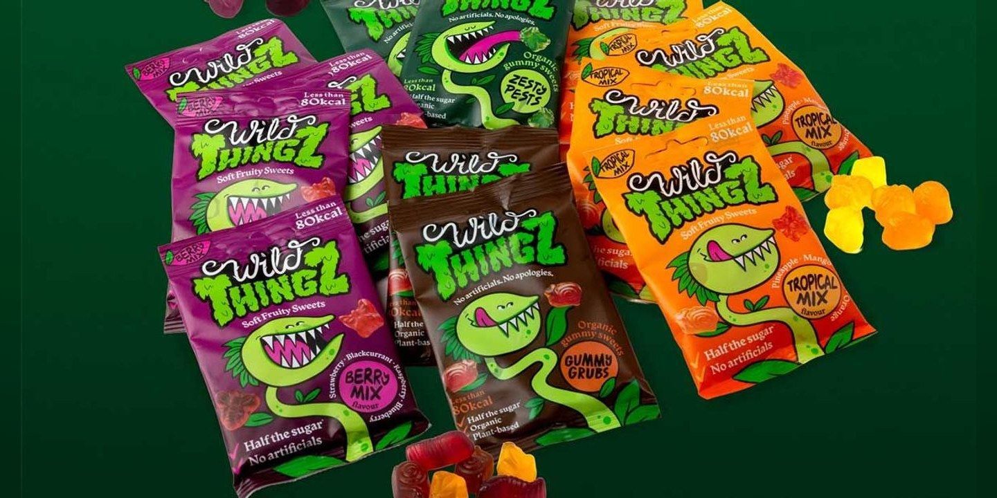 Bags of Wild Thingz sweets in Berry Mix, Tropical Mix, Zesty Pests and Gummy Grubs on a dark green background, with loose sweets