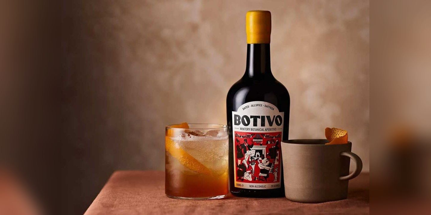 A bottle of Botivo Wintery Botanical Aperitivo between a glass with ice and orange peel and a ceramic mug garnished with orange peel