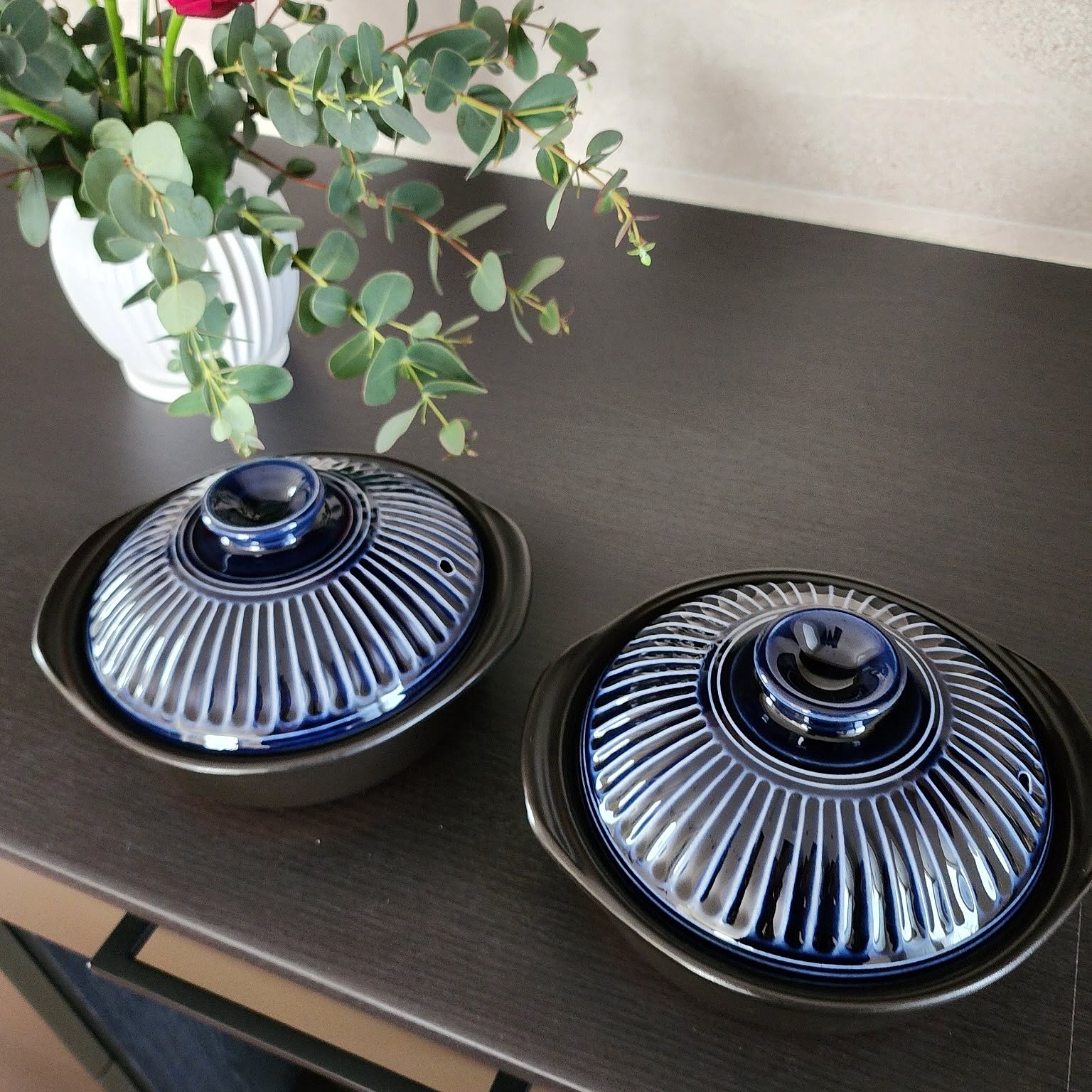 Two single-serving Japanese donabe with navy chrysanthemum lids on a dark wood sideboard