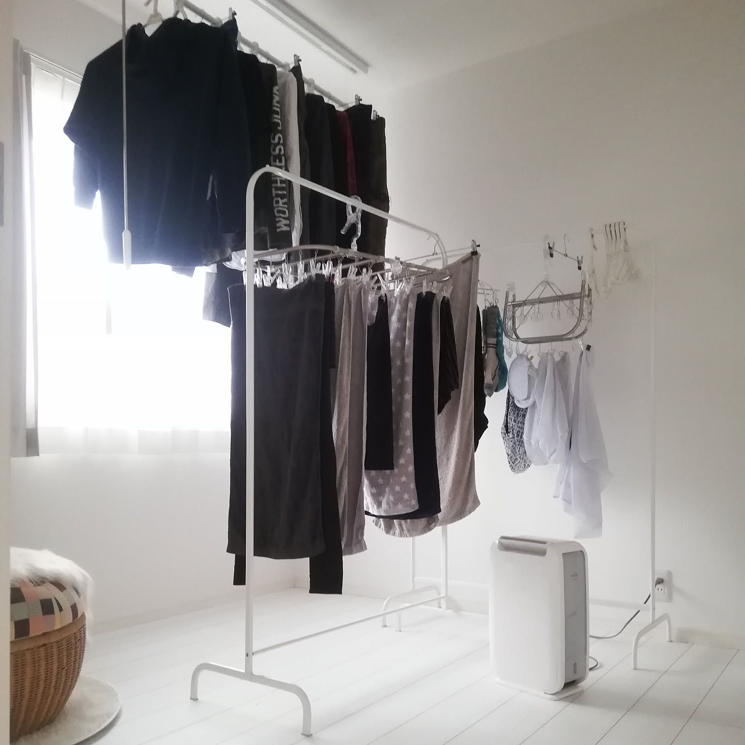 Indoor laundry drying on a freestanding rack beside a bright window and dehumidifier.