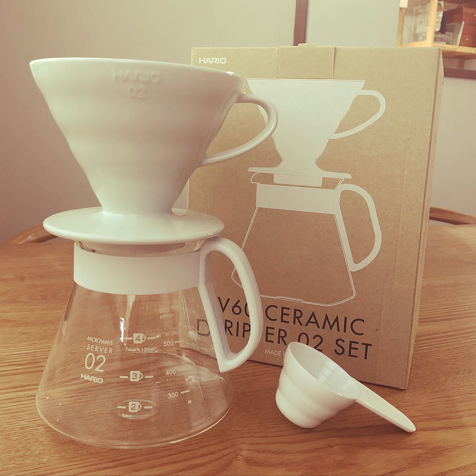 A white HARIO V60 ceramic dripper set on a glass server beside its box.
